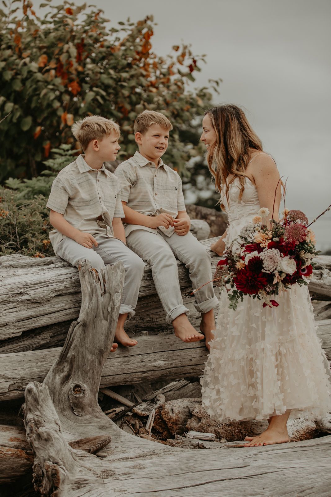 A casual beach wedding moment captured on driftwood with children and a beautiful bouquet.