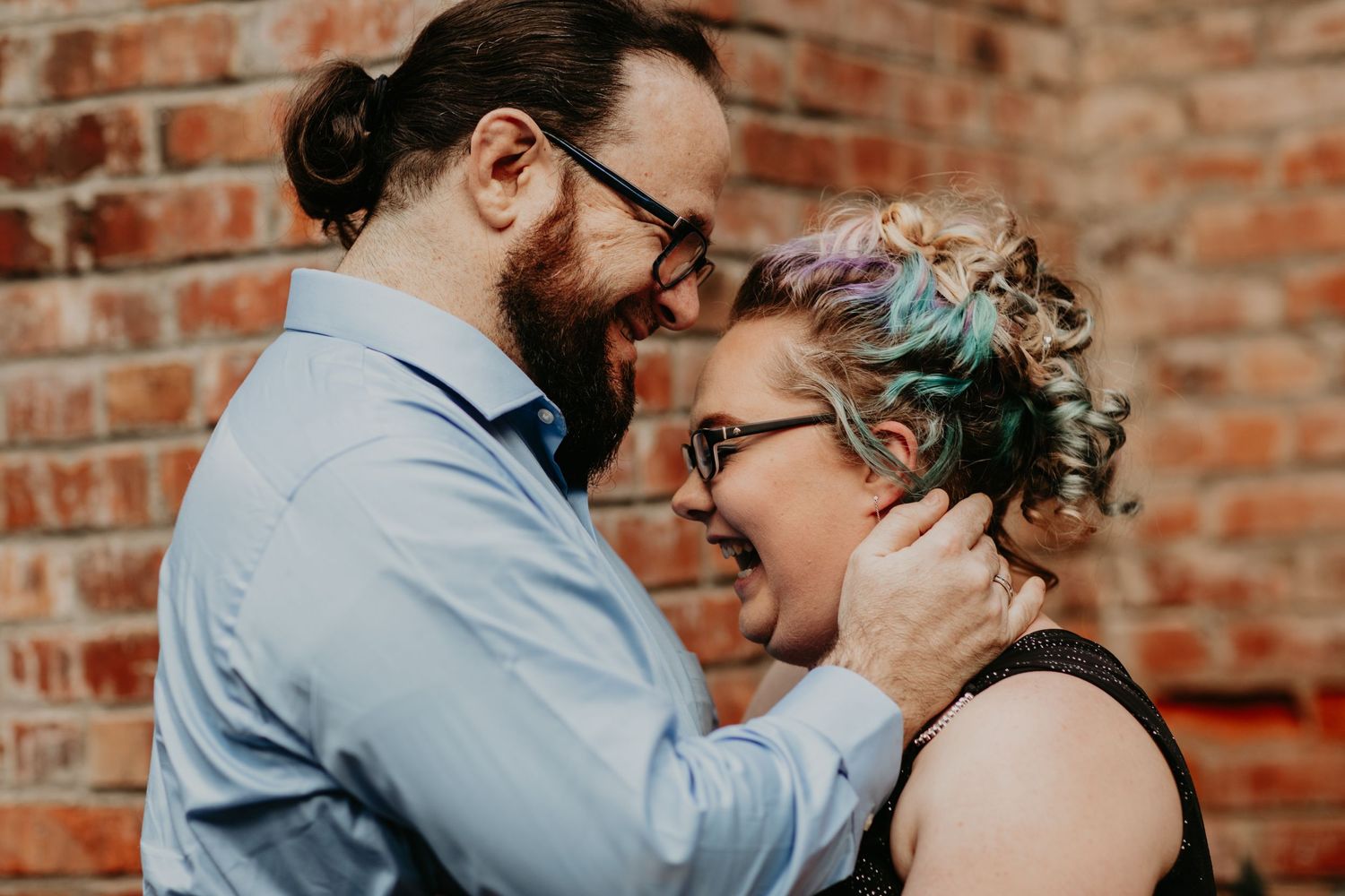Romantic couple sharing intimate moment against brick wall background.