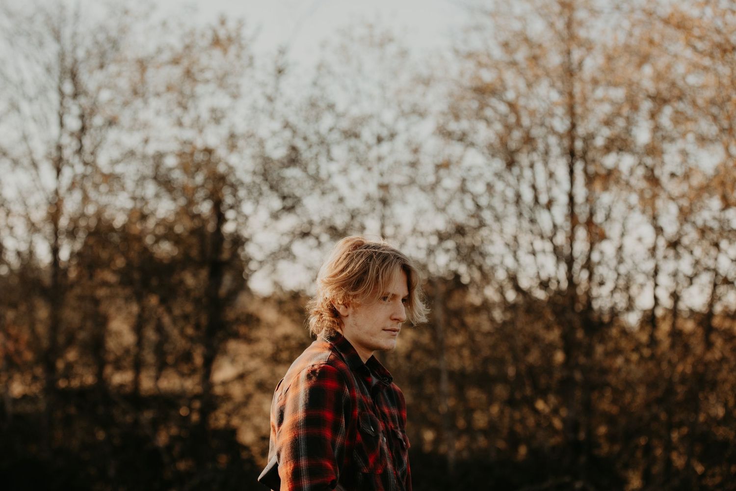 A moody outdoor autumn portrait at sunset with tall trees in the background.