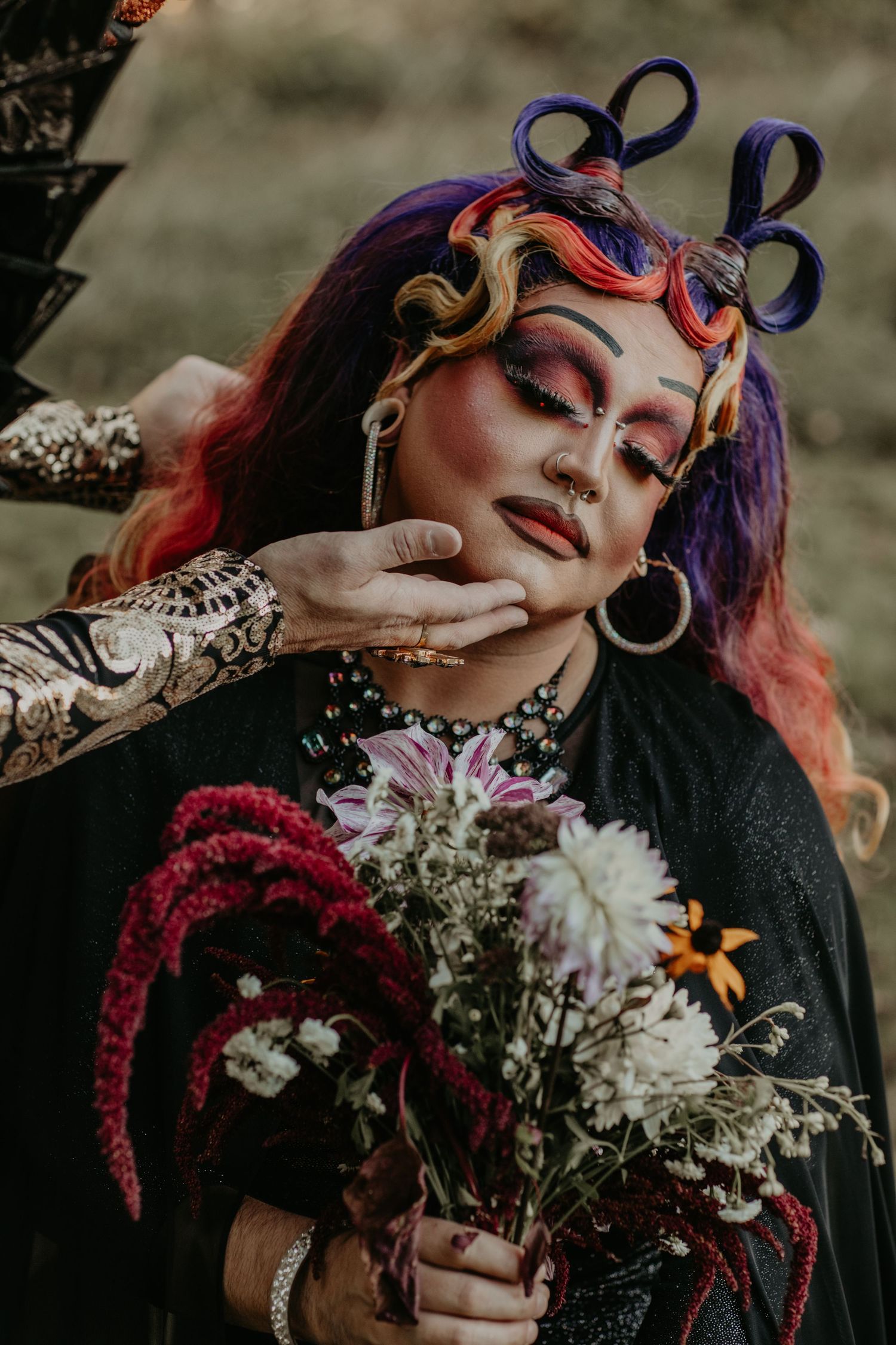 Creative portrait of a model with colorful hair holding a bouquet of flowers wearing gothic style makeup and accessories.