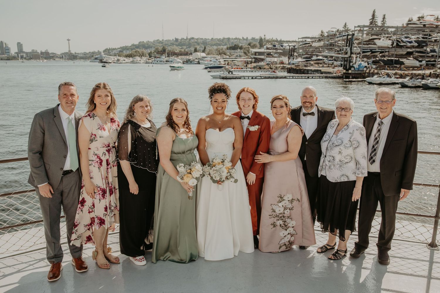 Wedding group photo with guests and wedding party on a waterfront dock with boats in view.