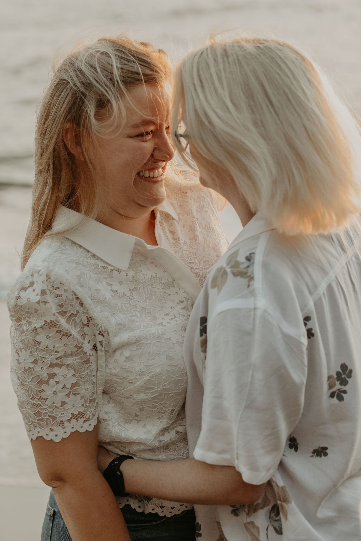 Two people share an intimate moment while wearing white lace and casual tops in warm sunset lighting.