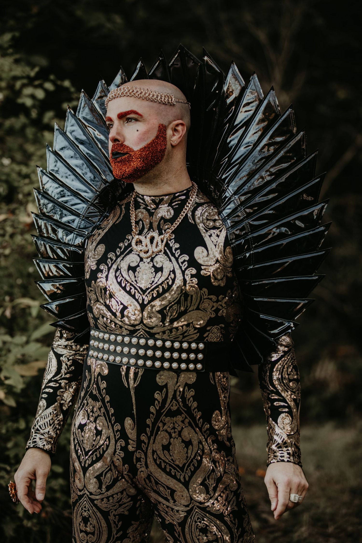 Dramatic fashion portrait featuring an ornate damask bodysuit and metallic spiked collar against a dark forest background.