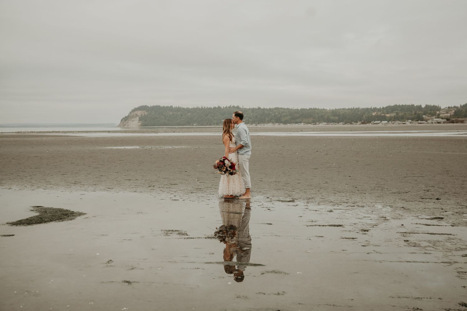 Person walking along a misty beach shoreline at low tide during an overcast day.