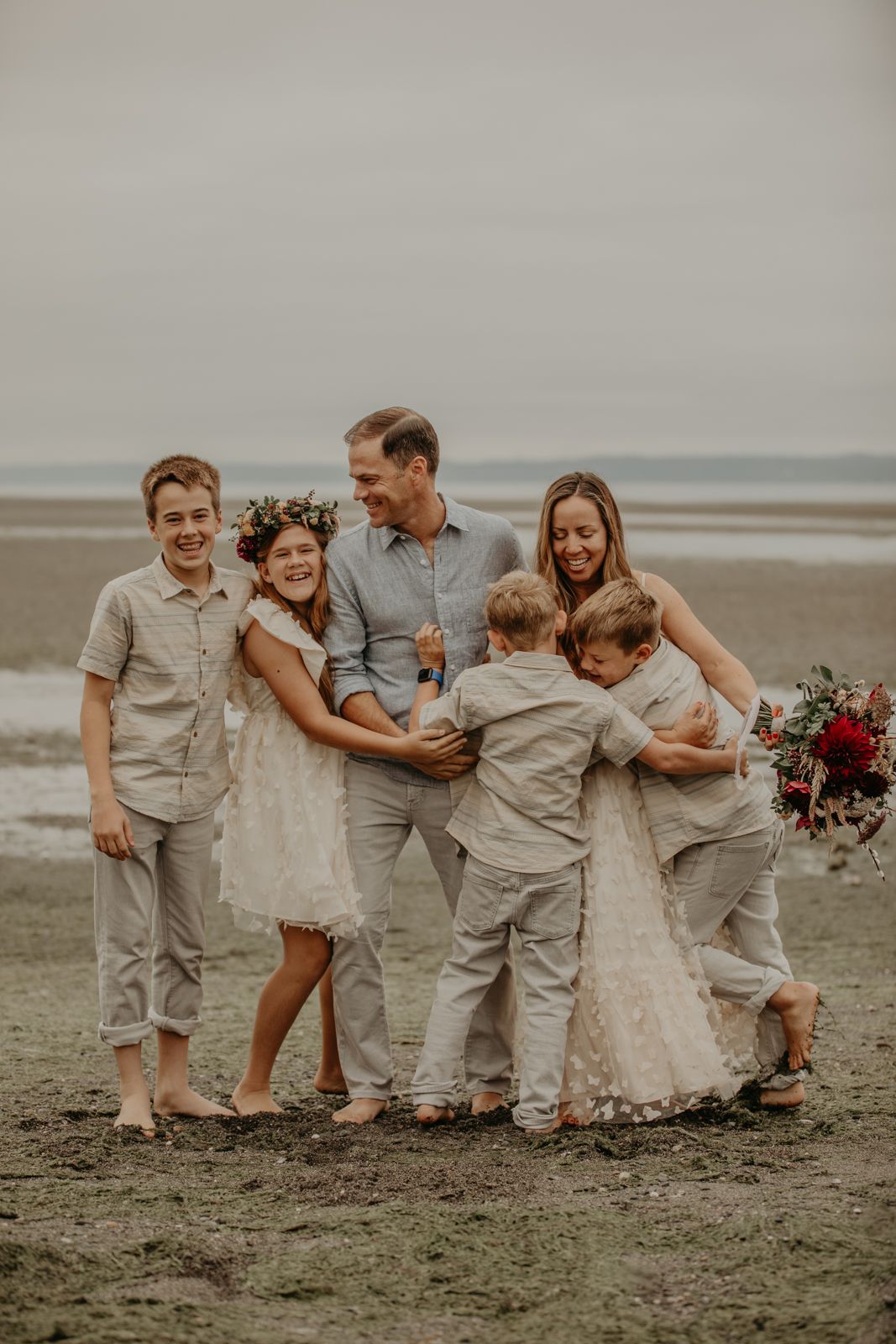 Family wearing coordinated beige and white outfits laughing together on a misty beach during a photo session.