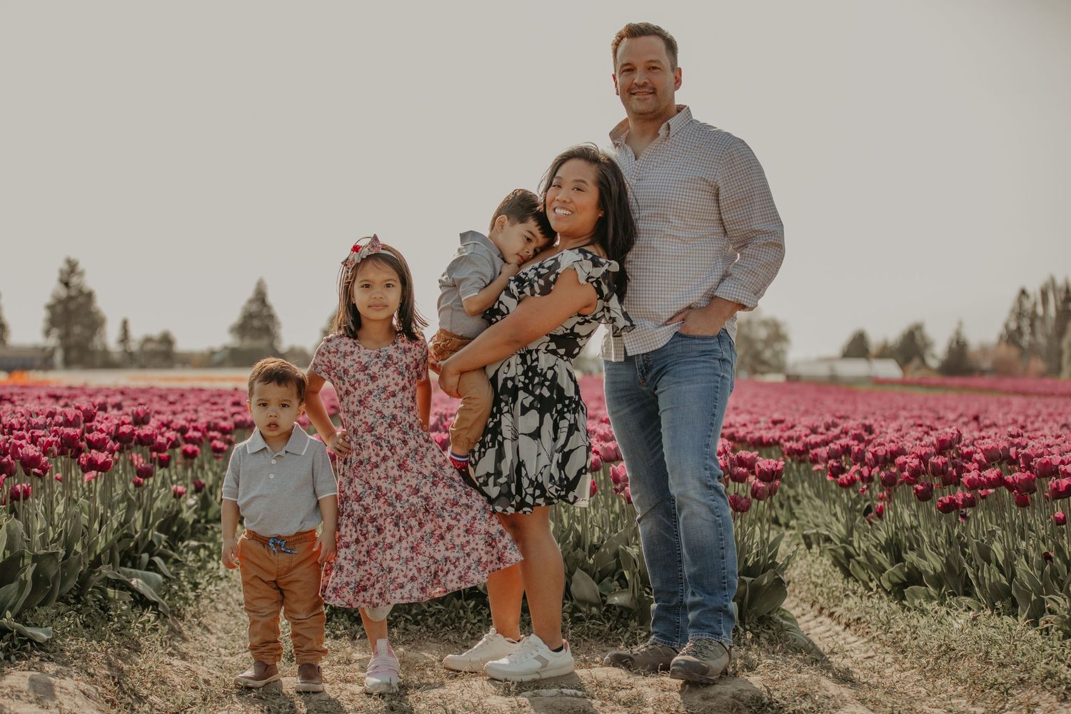 A family poses together in a vibrant tulip field filled with pink blooms on a sunny afternoon.