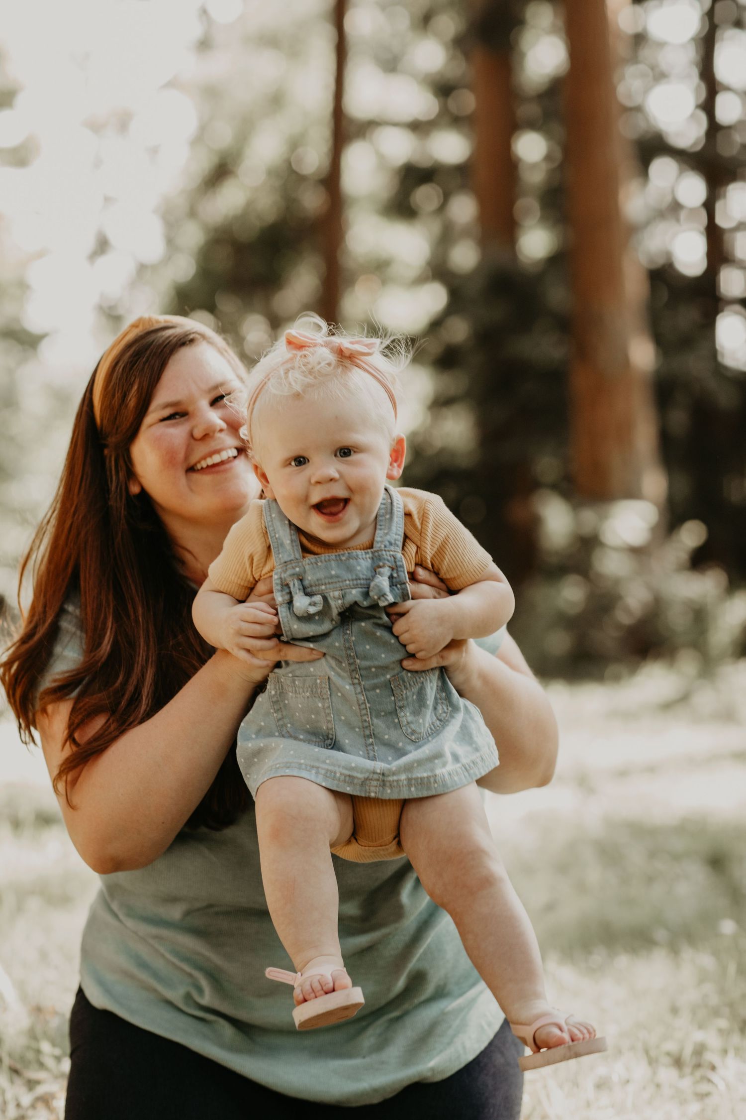 A joyful moment captured in a sunlit forest as two people share laughter outdoors during a warm afternoon.
