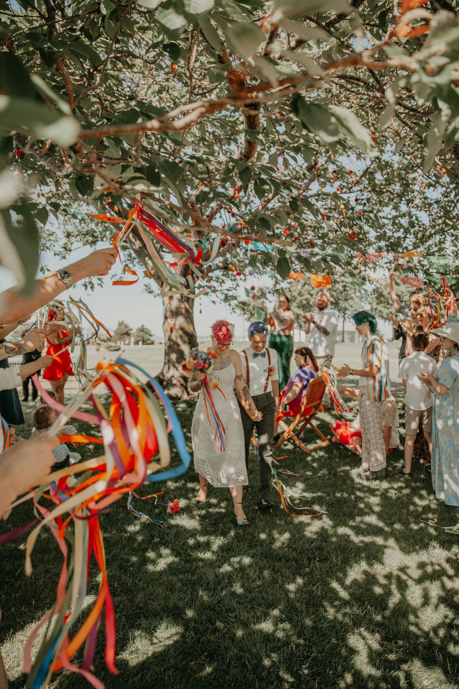 Colorful ribbons and decorations hanging from tree branches create a festive outdoor celebration atmosphere.