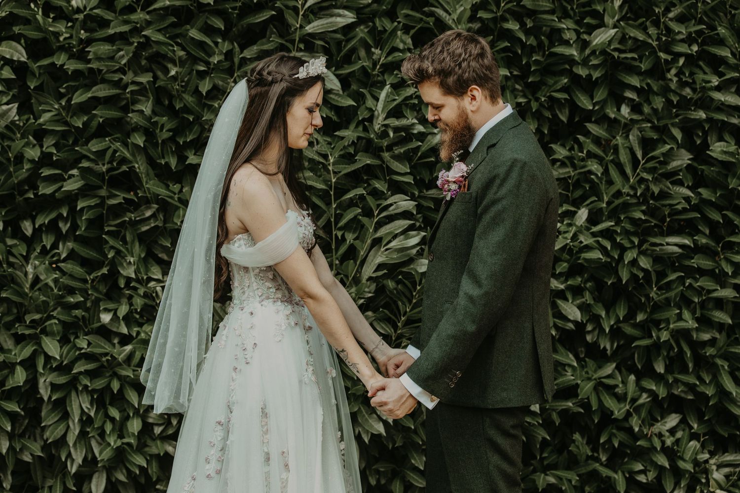 A couple shares an intimate moment against a lush green hedge wall during their wedding ceremony.