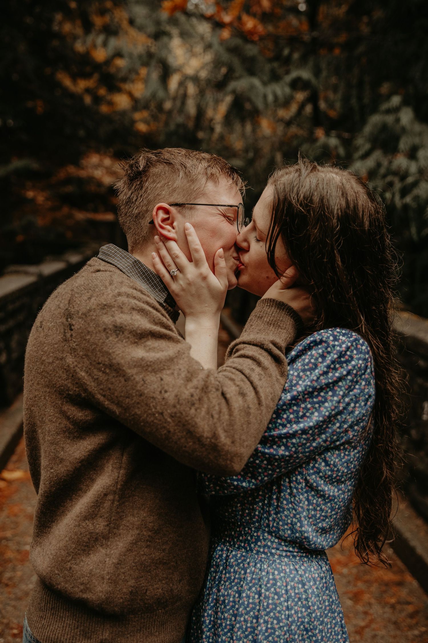 A romantic autumn scene shows a couple sharing a tender kiss in a forest with orange fall foliage in the background.