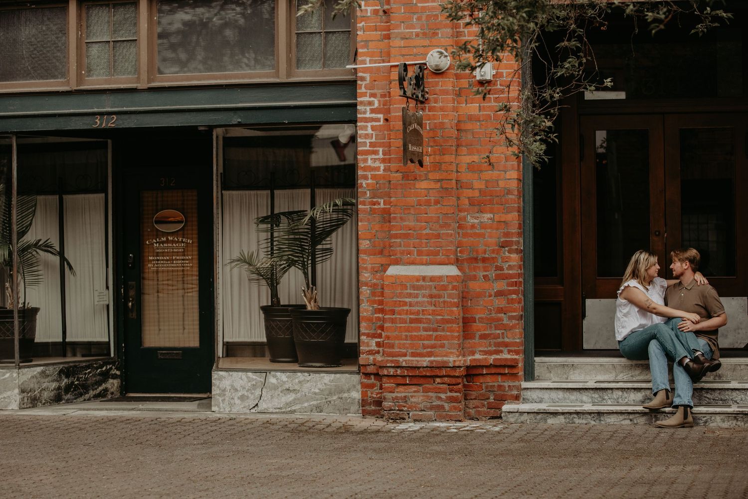 A couple shares a romantic moment while sitting outside a historic brick building.