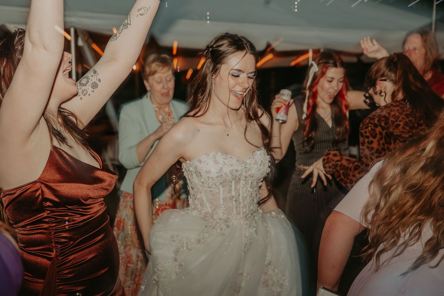 Wedding guests dance and celebrate on a dimly lit dance floor during an energetic reception party.