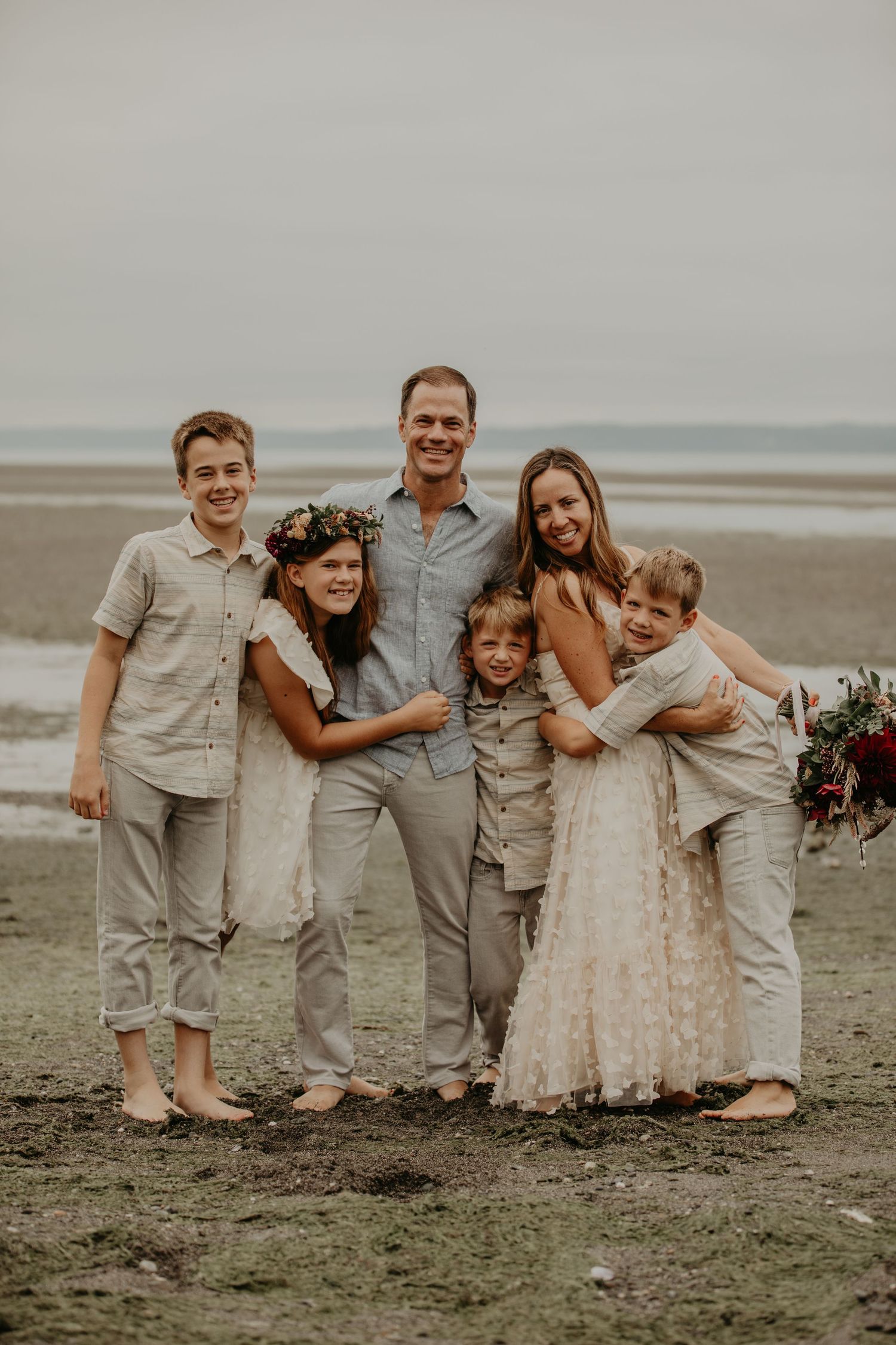 Family group poses together on moody beach wearing coordinated neutral colored outfits.