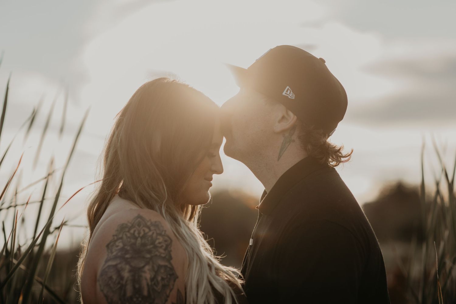 Silhouetted couple sharing an intimate moment in a field at sunset with sun rays backlighting the scene.