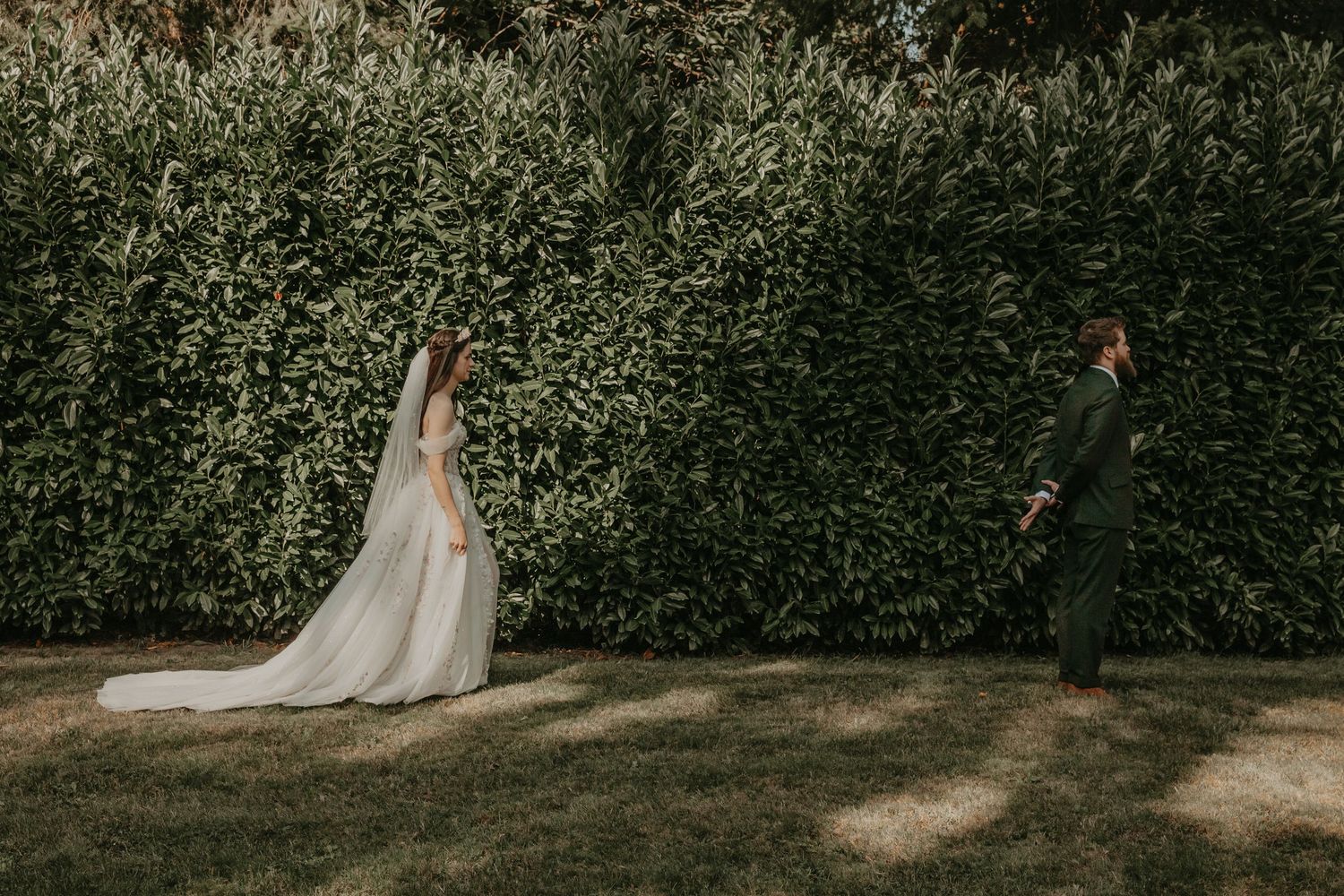 A bride in a flowing white gown stands elegantly in a garden setting with lush greenery creating a natural backdrop.