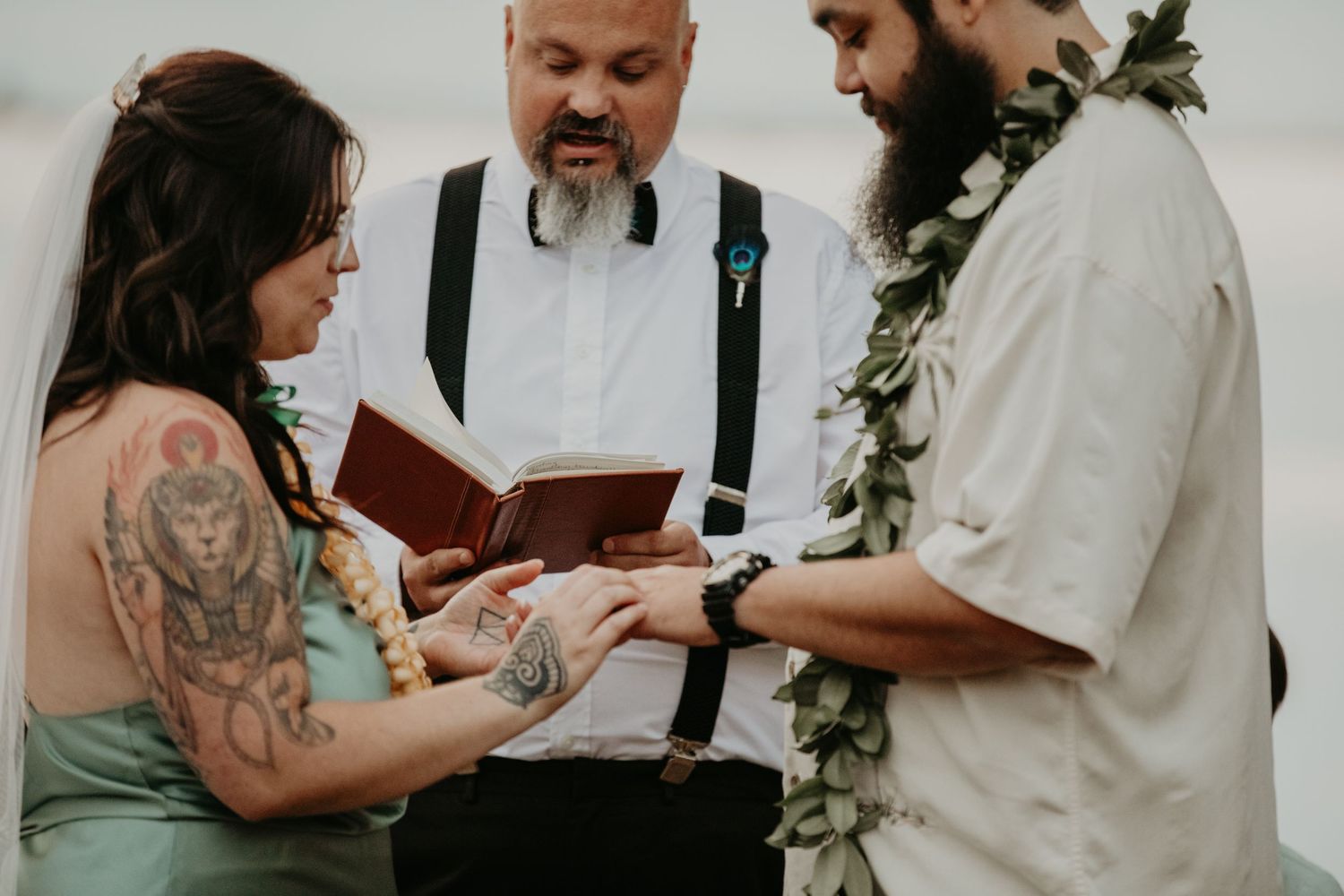 A wedding ceremony showing exchange of rings with an officiant in suspenders reading from a book during intimate ceremony.