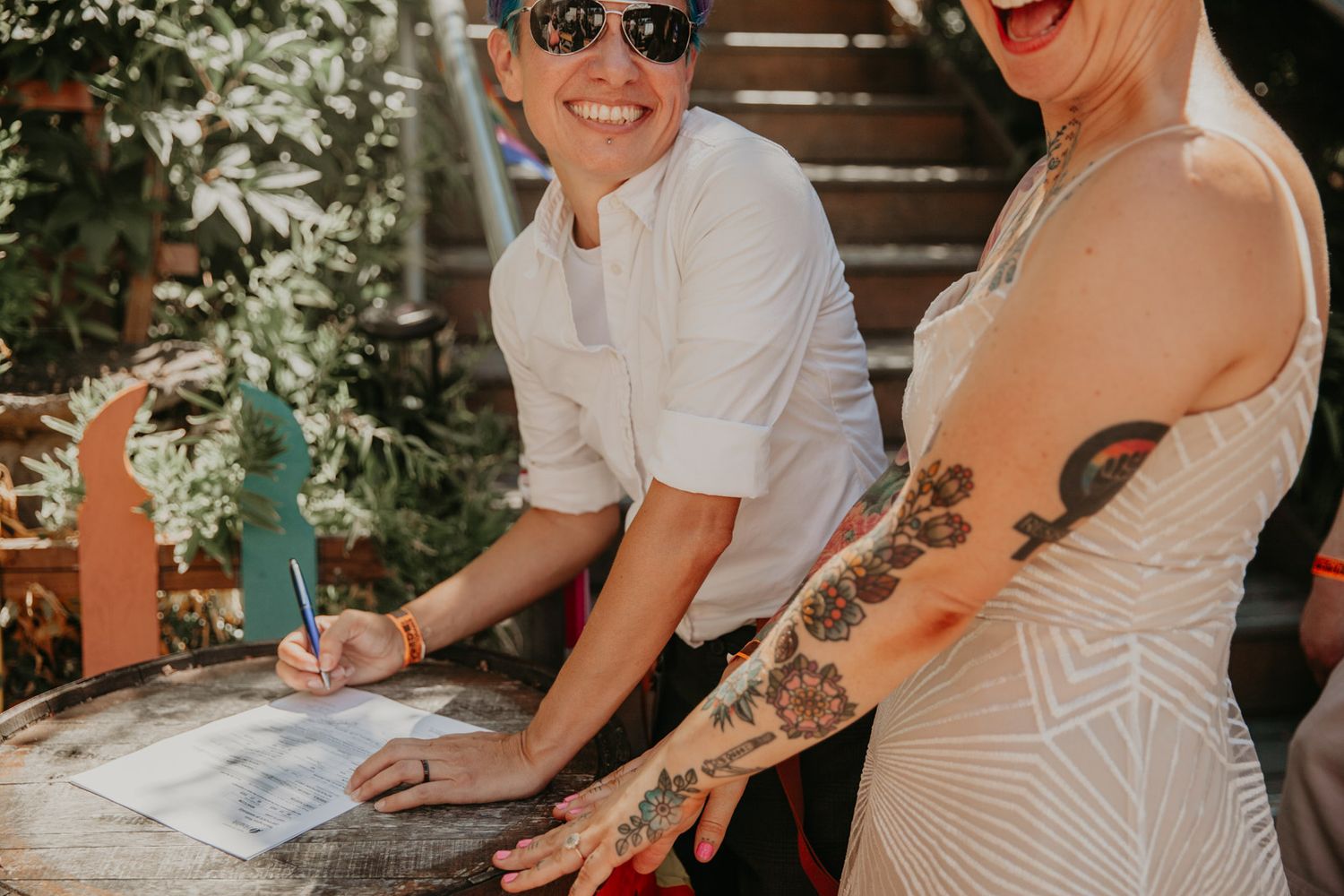 Wedding guests sign the marriage certificate with smiles and laughter during an outdoor ceremony.