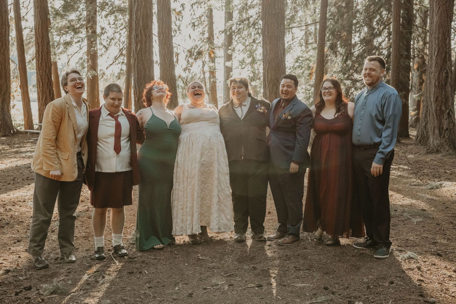 Large wedding party group photo taken in a scenic forest setting with tall trees in background.