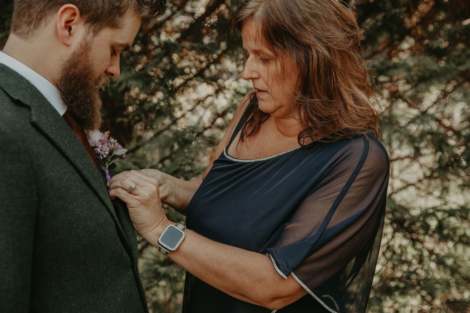 Someone pins a boutonniere flower to a green suit jacket during an outdoor event.