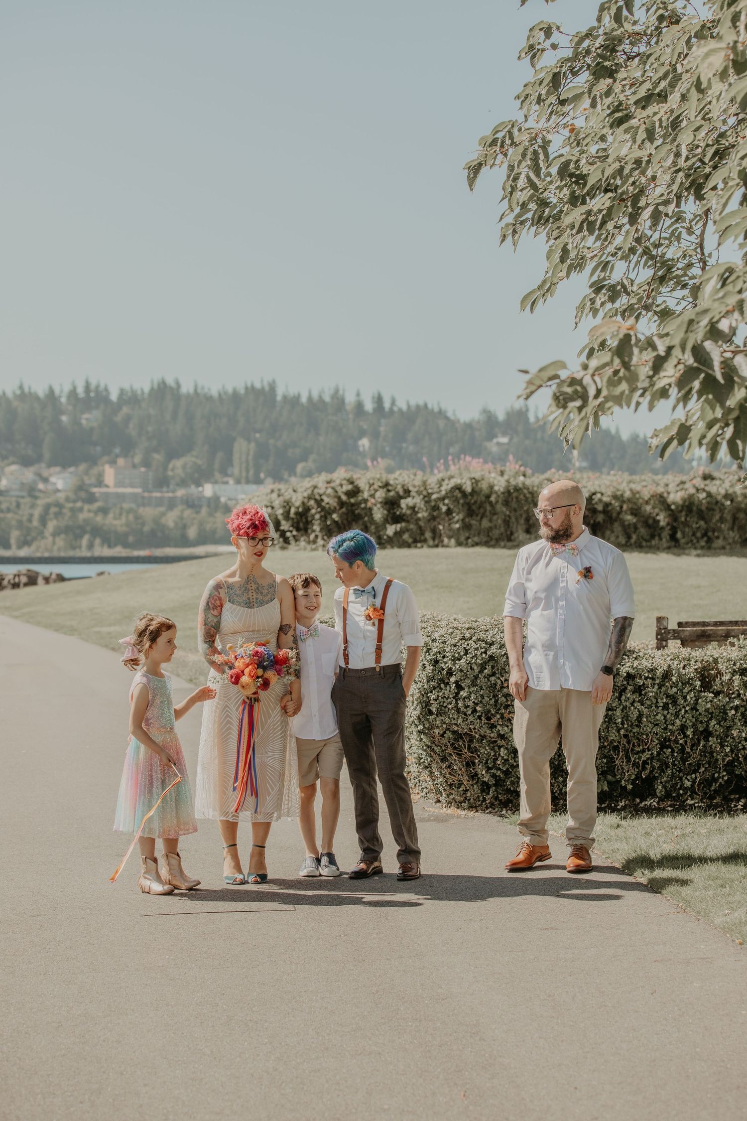A small wedding party stands together on a scenic pathway overlooking water and trees.