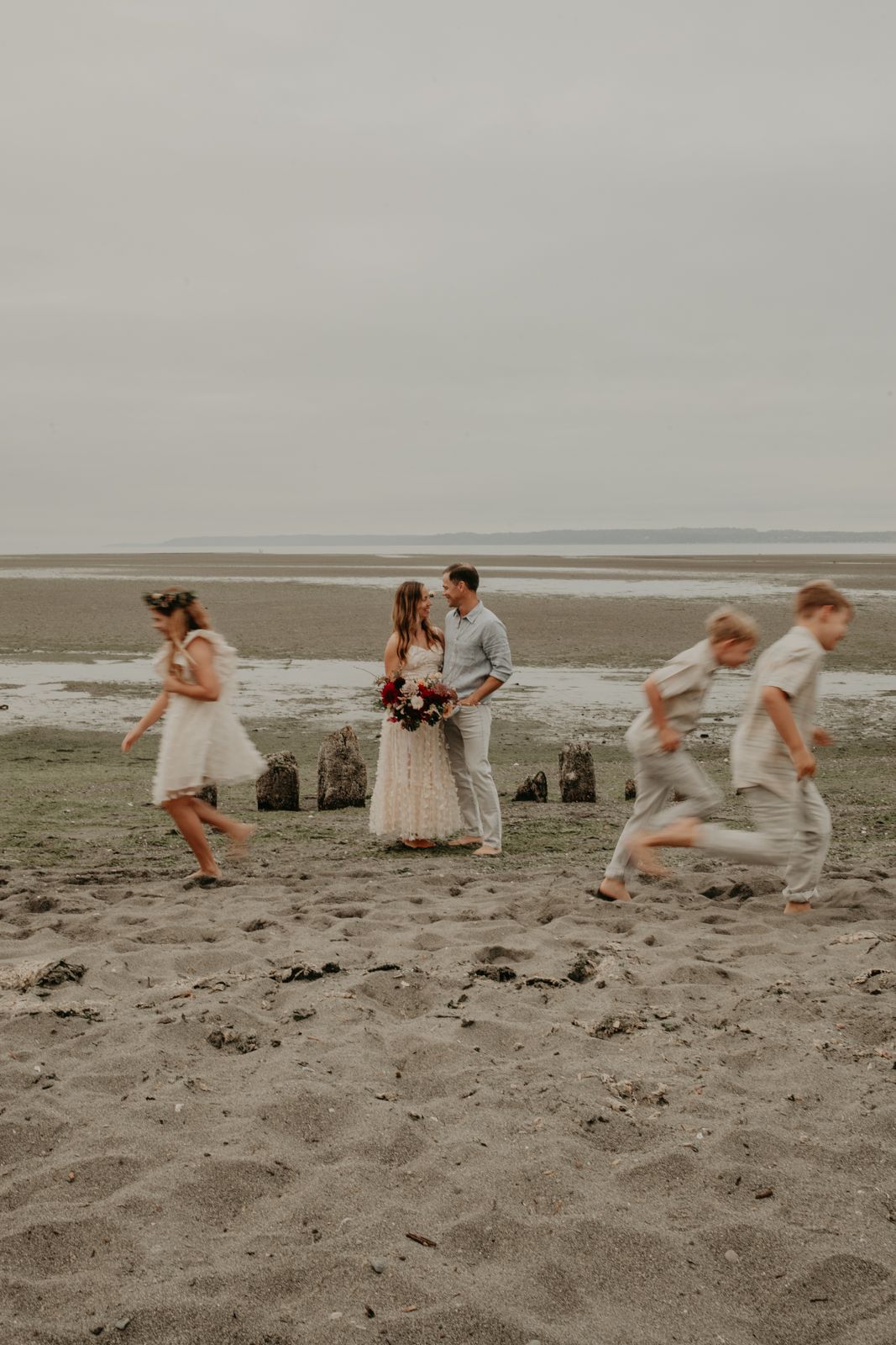 Candid beach wedding photo showing people running and playing on sandy shores.