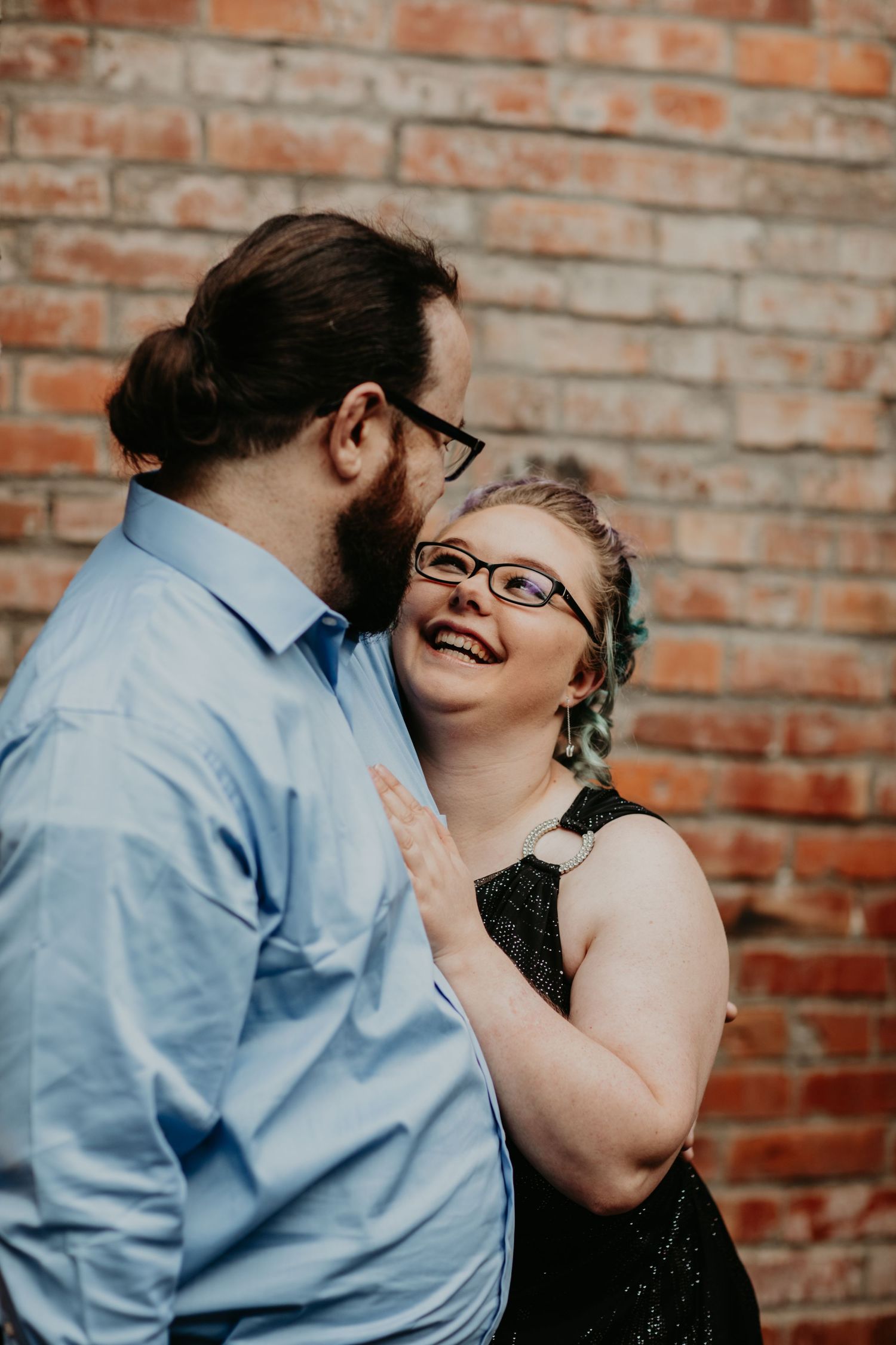 Two people share a joyful moment together while dressed in blue and black against a brick wall backdrop.