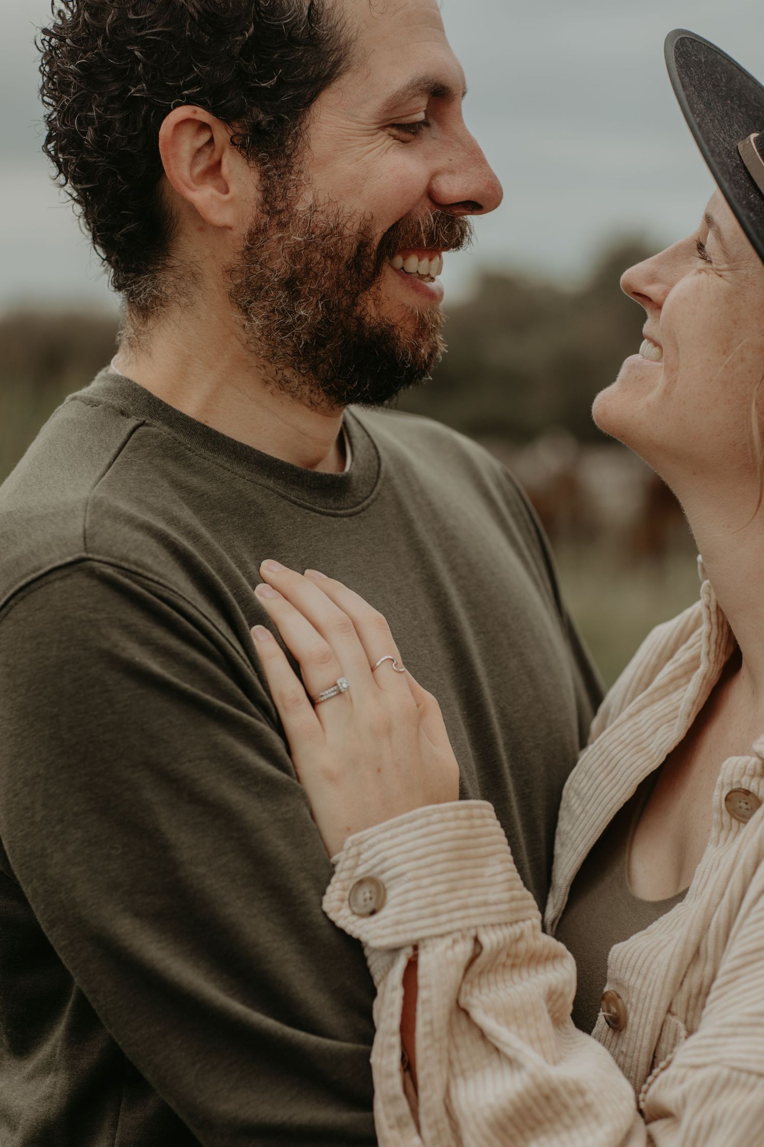 A romantic couple shares a joyful moment together outdoors, with one wearing a brown sweater and the other in beige.