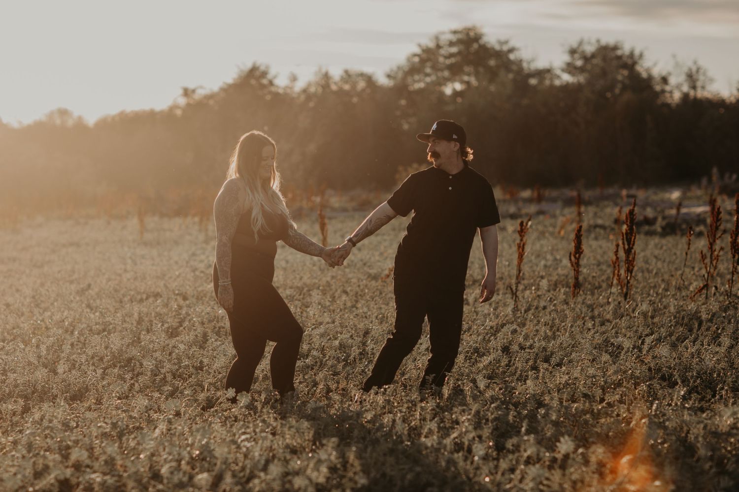 Couple holding hands while dancing together in a golden sunlit meadow at sunset.