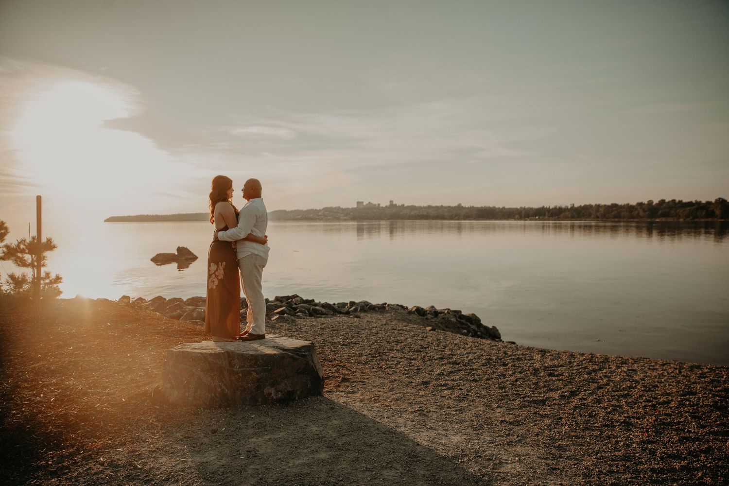 Two silhouettes embrace on a romantic beach at sunset, their figures casting long shadows on the sandy shore.