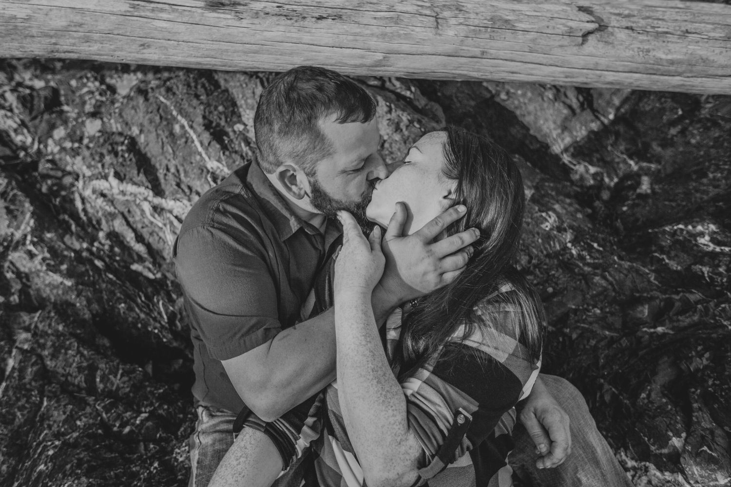 A black and white intimate portrait of a couple sharing a tender moment against rocky backdrop.