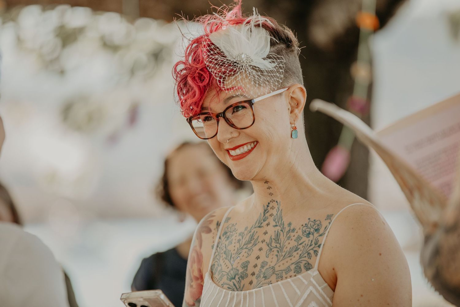 A floral crown made of red and pink flowers adorns someone at an outdoor celebration.