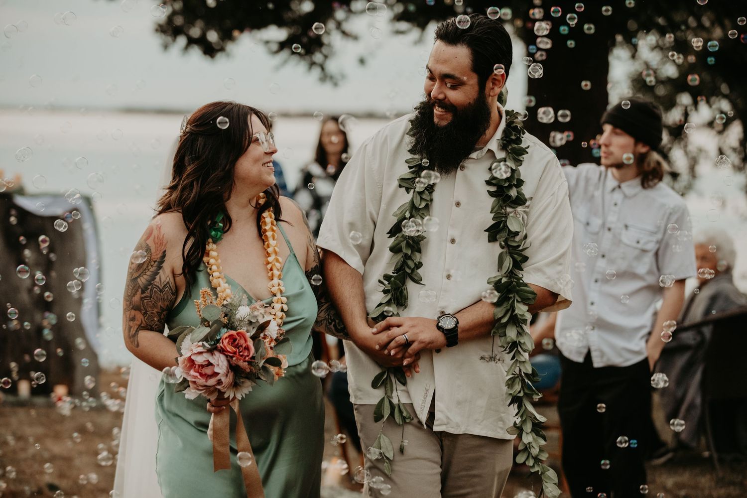 Couple at tropical wedding ceremony with bubbles floating in the air and tropical greenery decorations.