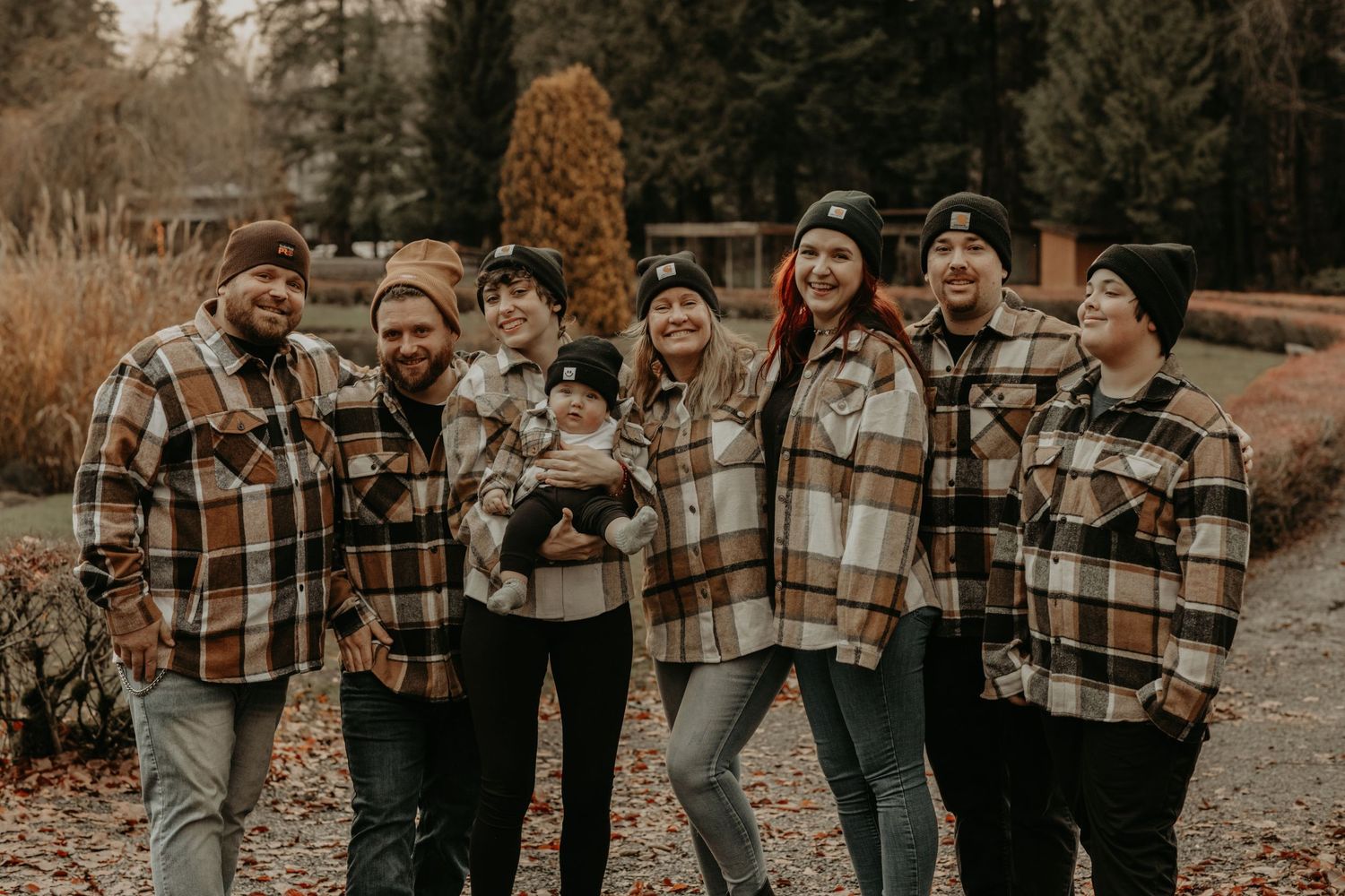 Group in matching plaid jackets poses together outdoors on an autumn day in a rustic woodland setting.