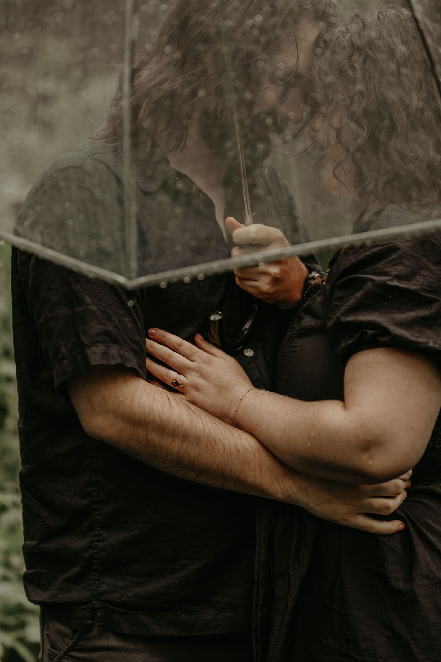 Two people sharing an intimate moment under a clear umbrella in nature.