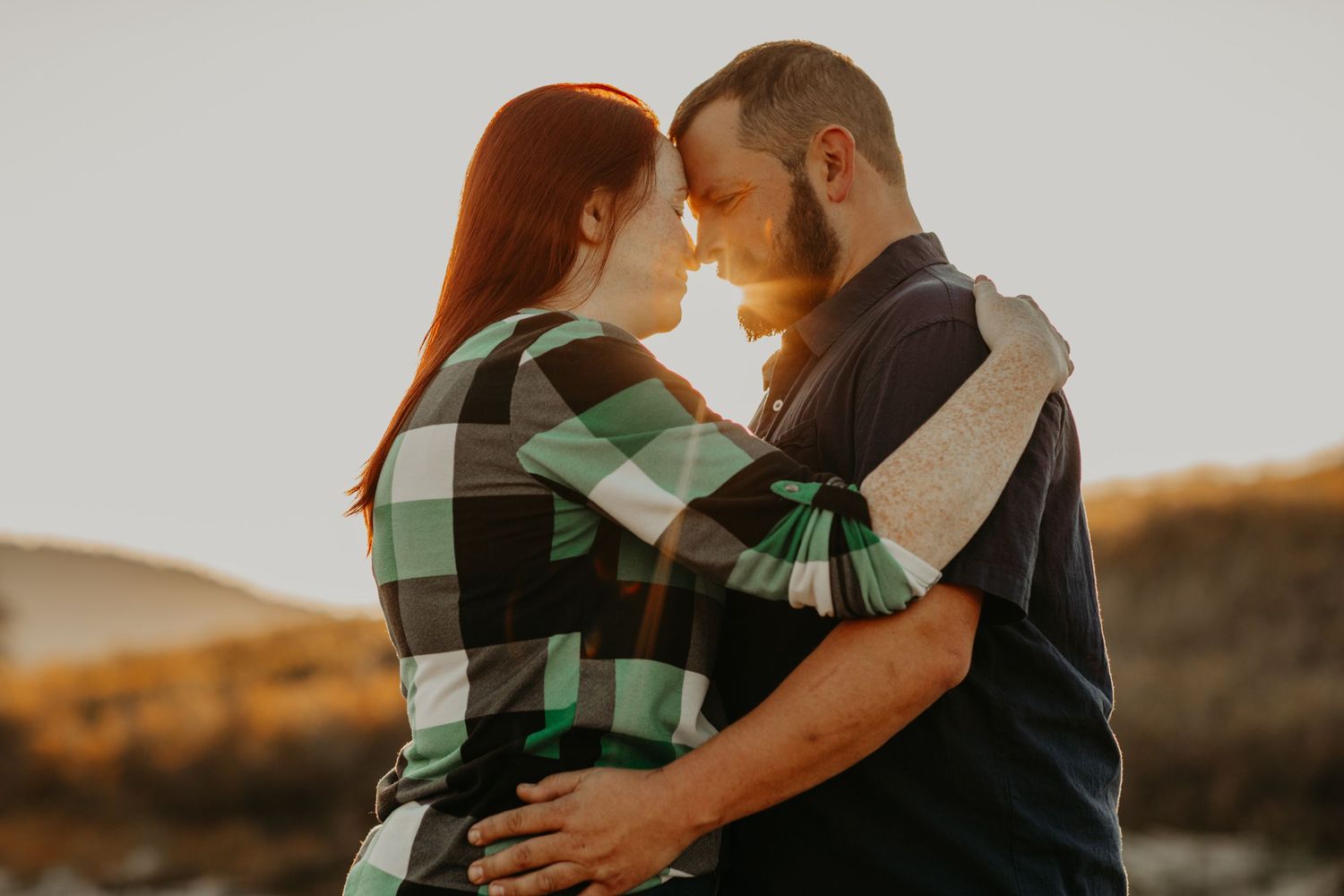 Couple in matching plaid shirts share intimate moment at golden hour sunset in outdoor setting.