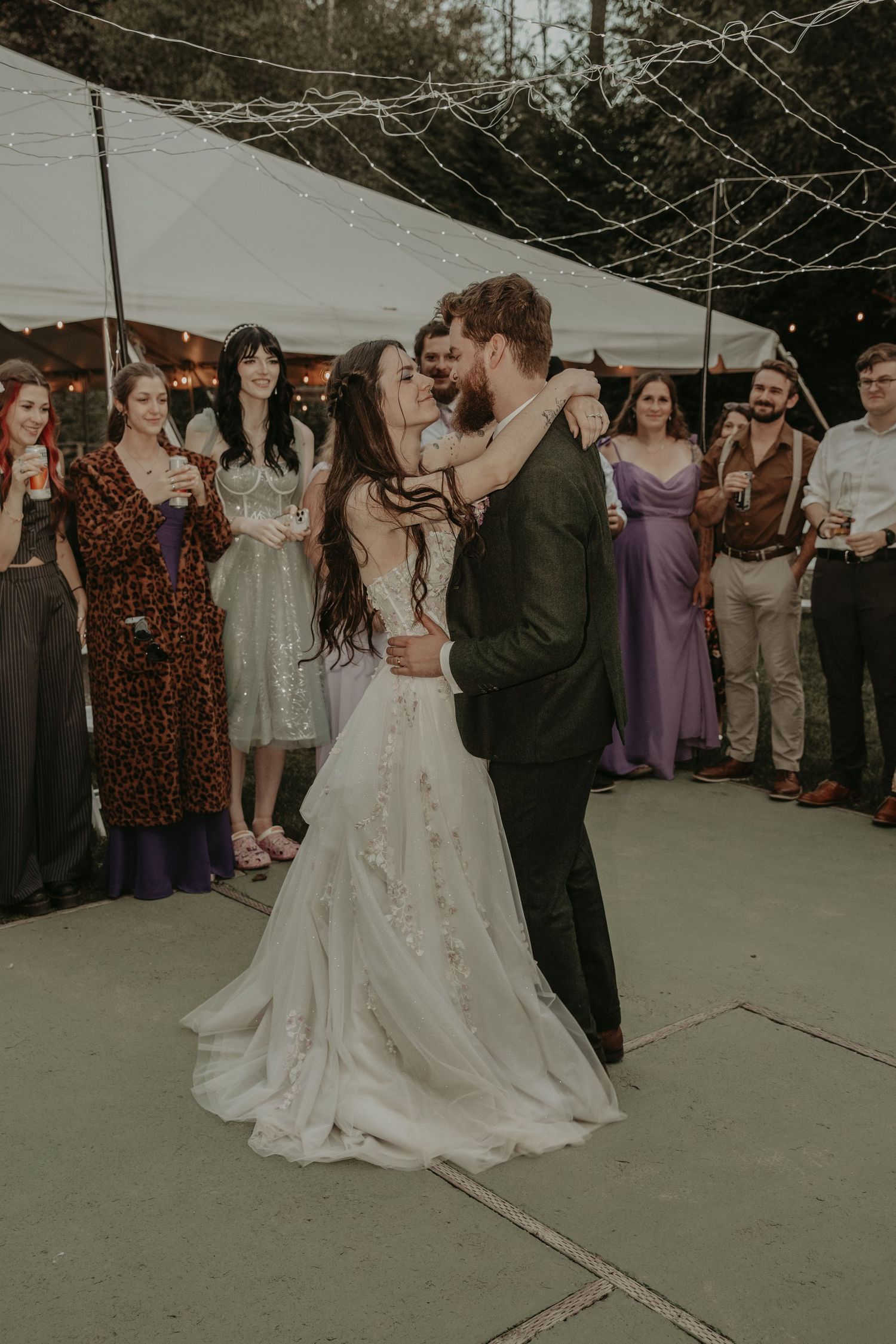 A couple dances together at an outdoor wedding reception as guests watch from the sidelines.