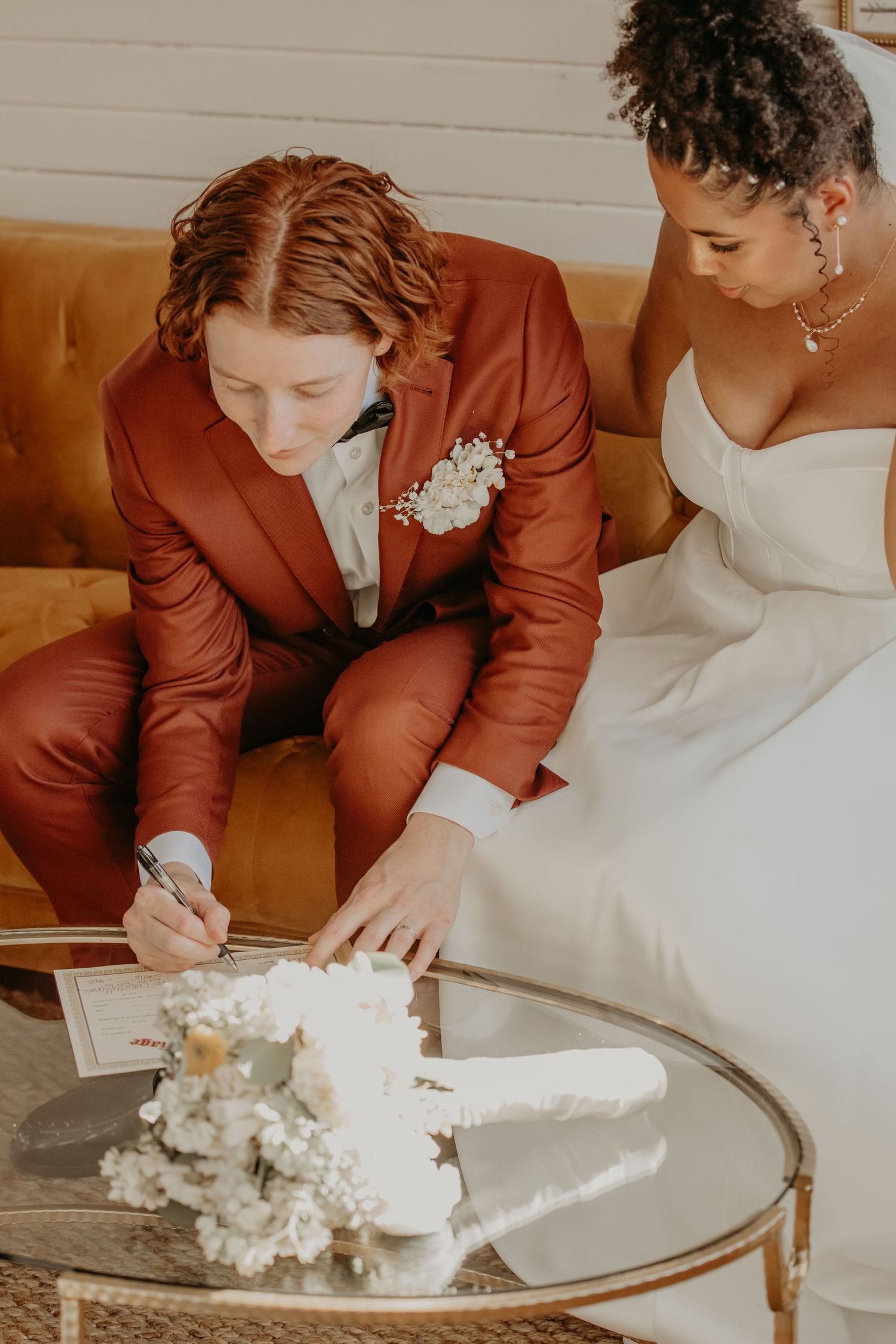 Wedding couple signing documents together on a brown leather couch.