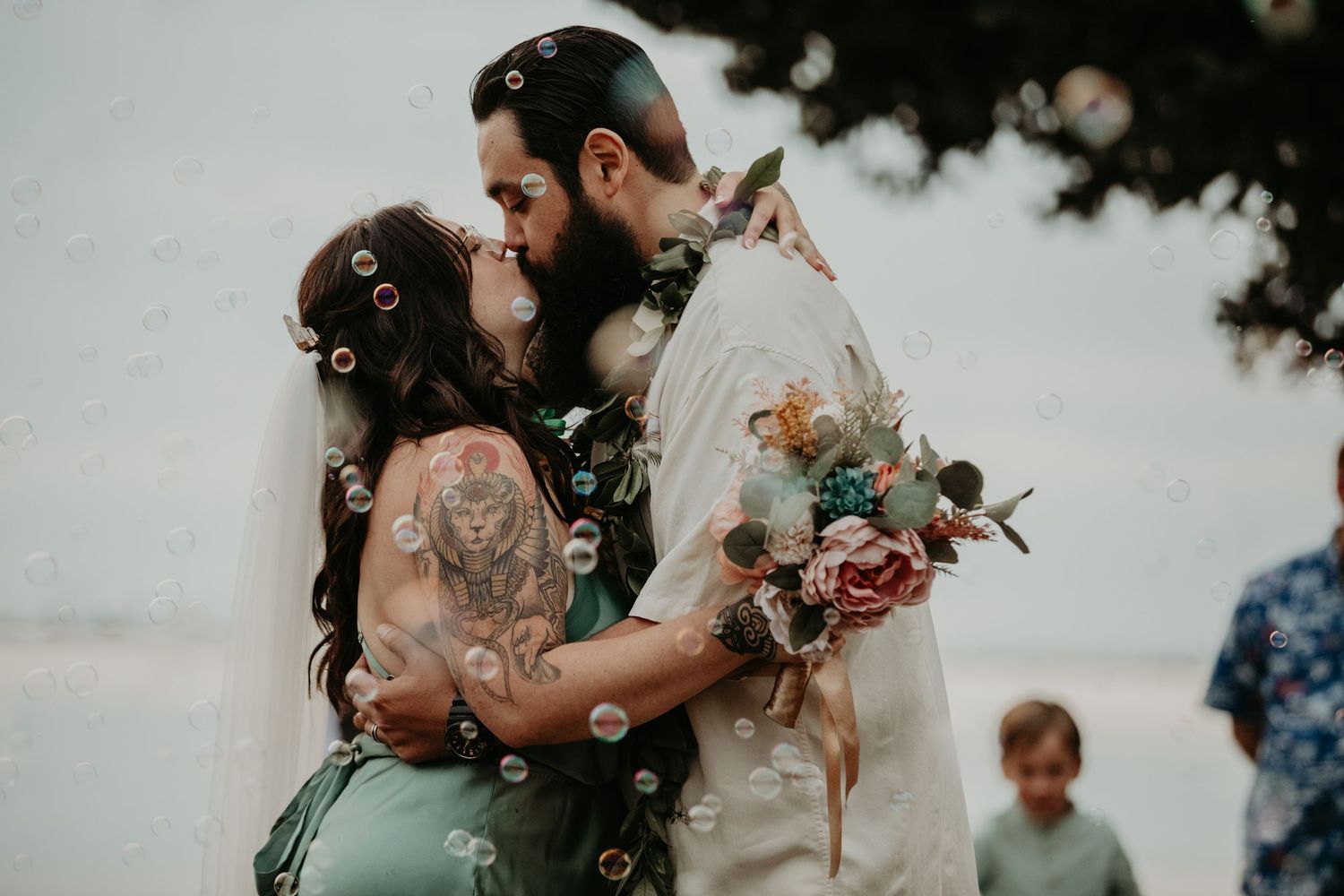 A couple embraces in an intimate pose outdoors holding a floral bouquet during a romantic wedding ceremony.