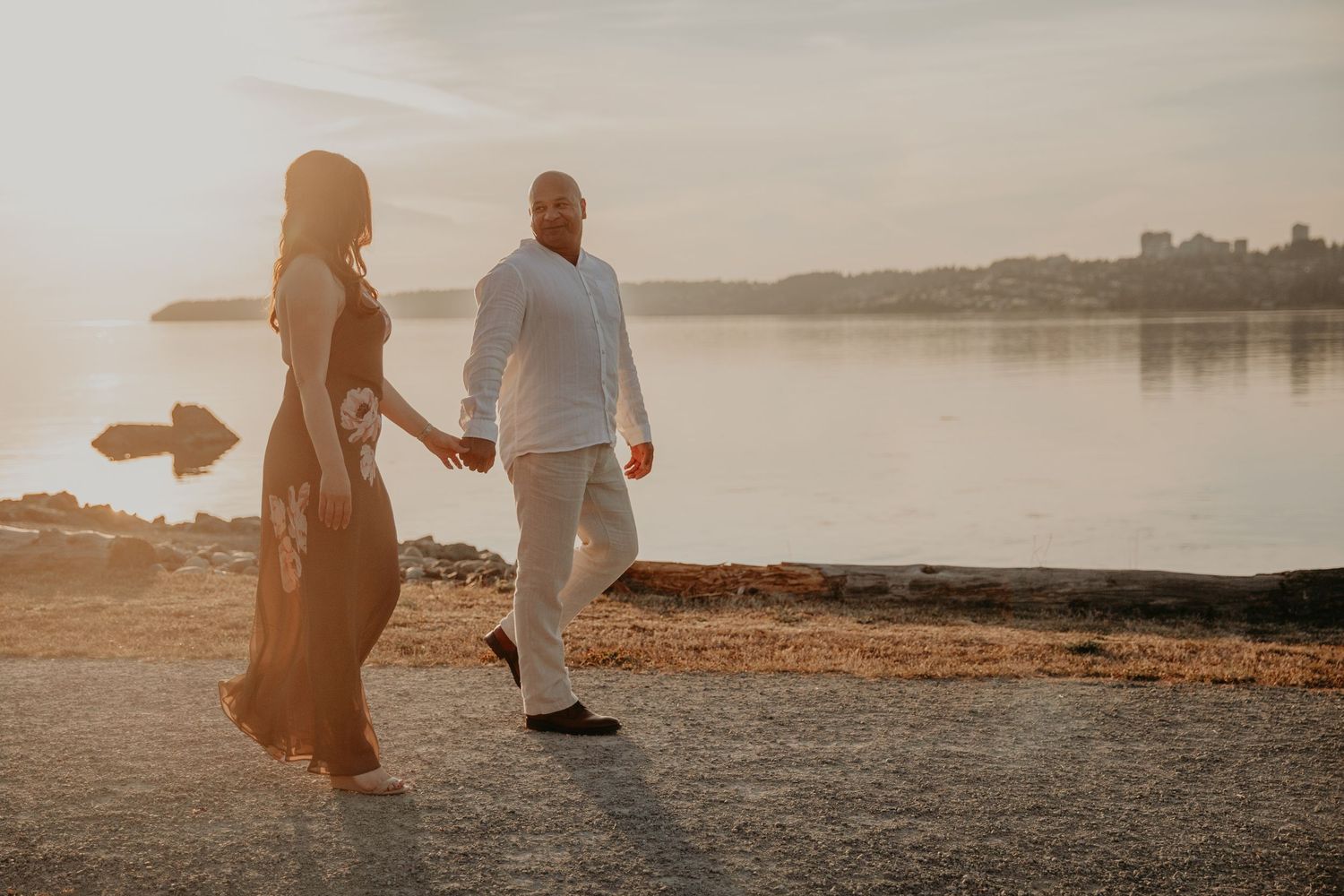 Two people walking along a serene lakeside path at sunset with golden light illuminating the peaceful scene.