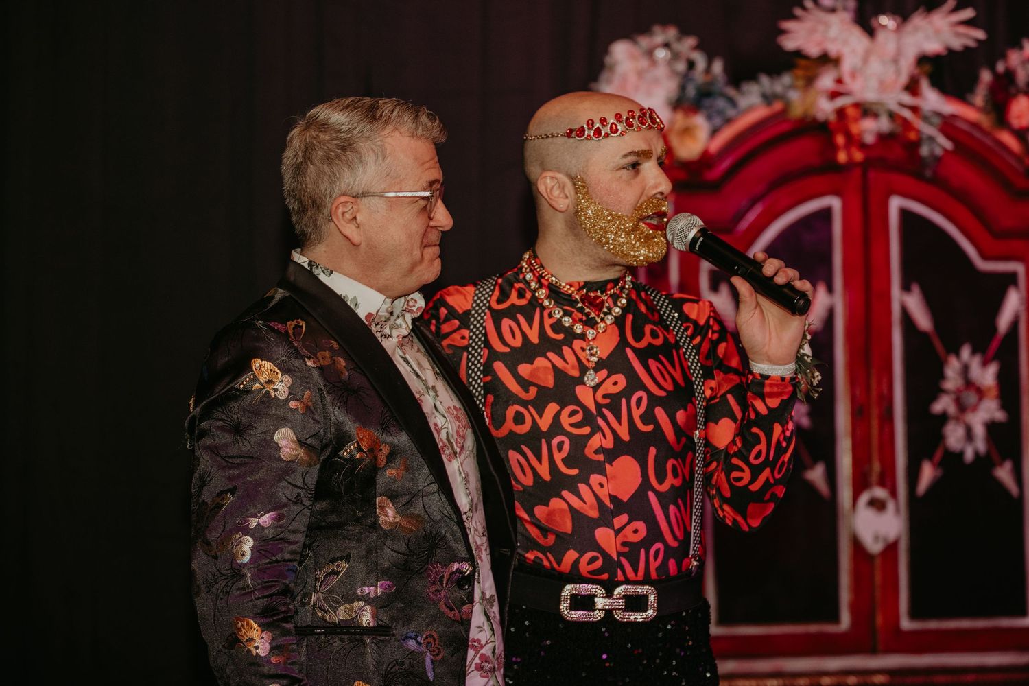 Two performers on stage wearing colorful outfits sing together during a live music performance.