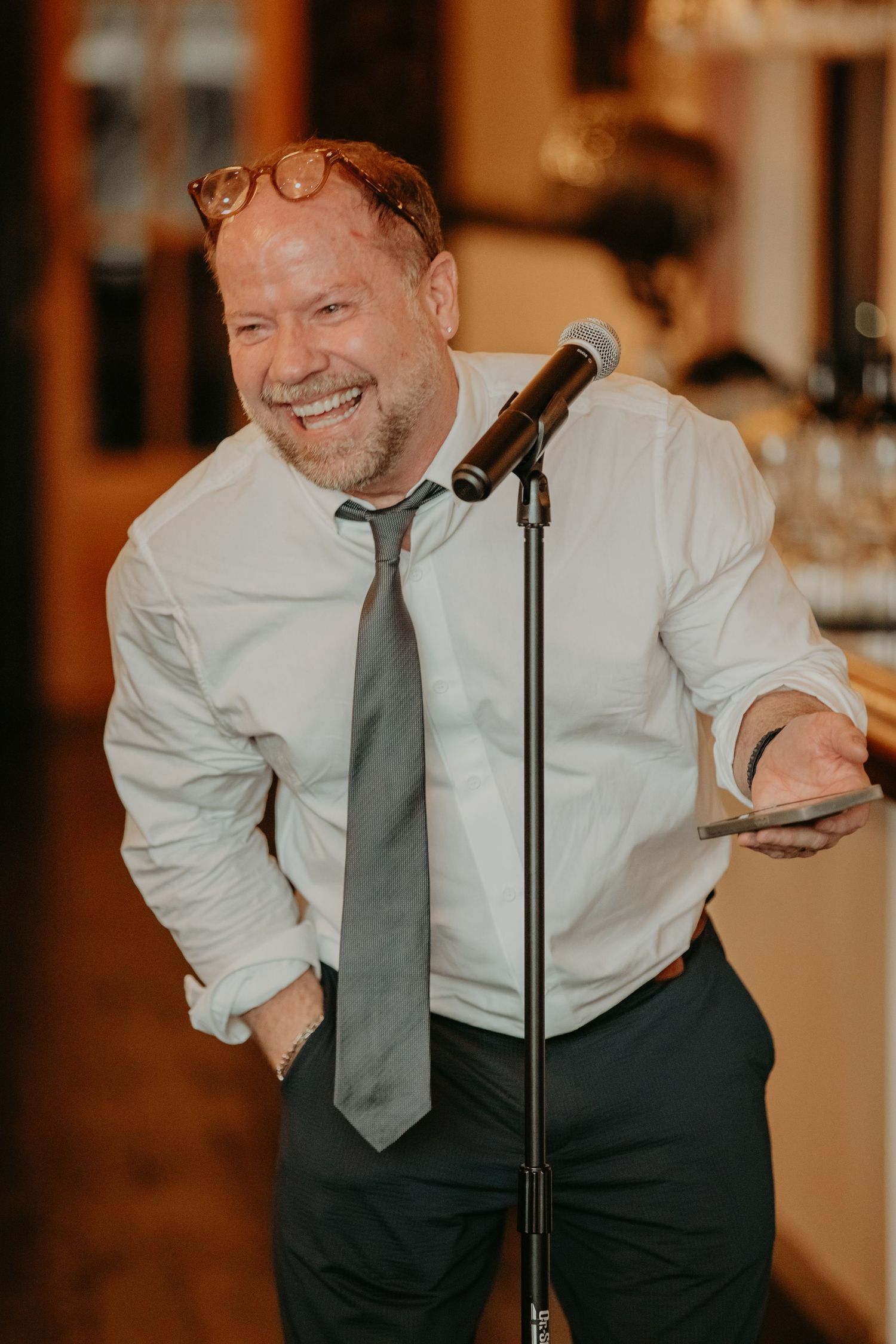 A person in formal attire performs energetically at a wedding reception with a microphone.