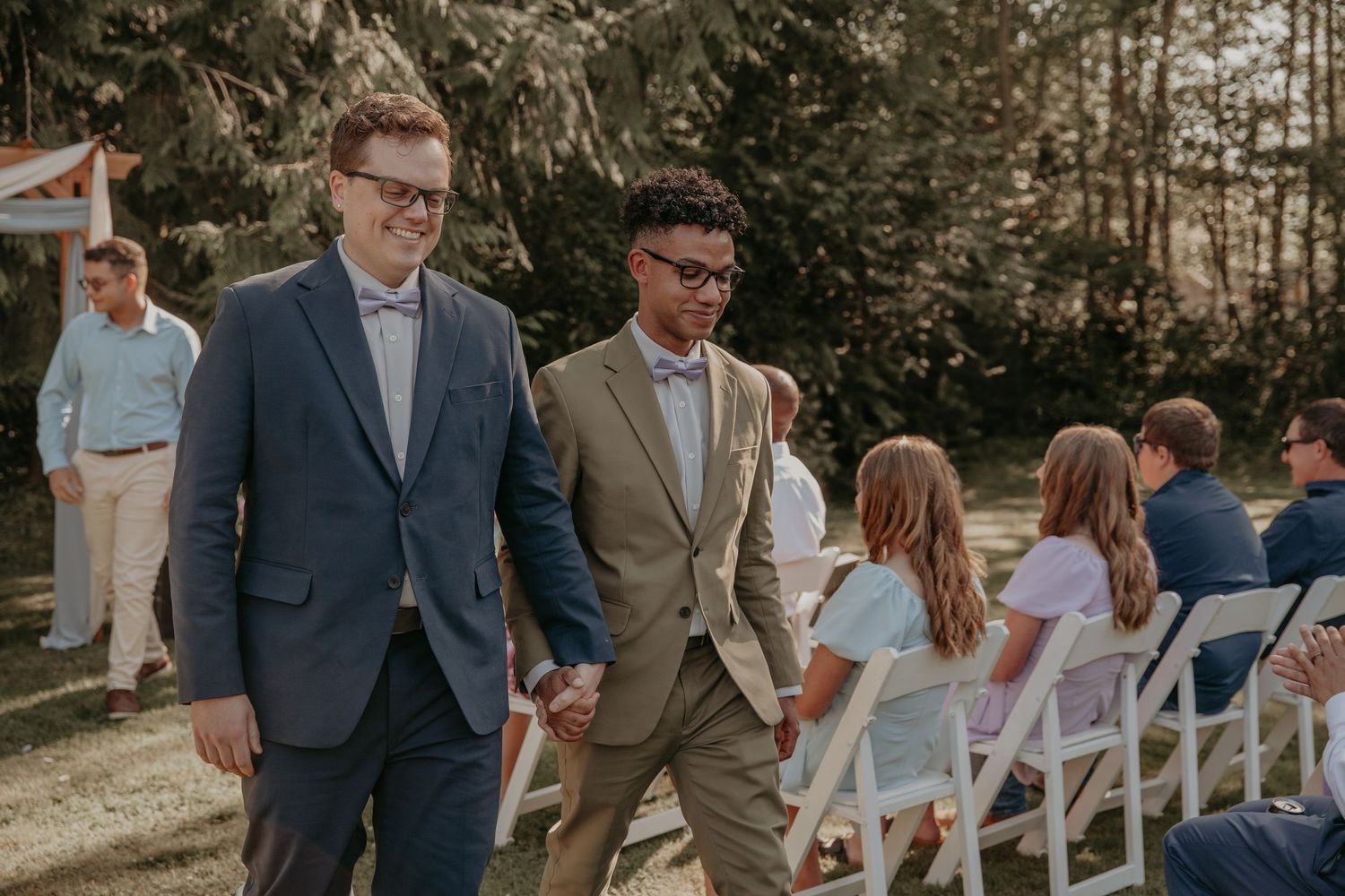 Wedding guests socializing at an outdoor evening reception with wooden chairs and string lights creating a rustic ambiance.