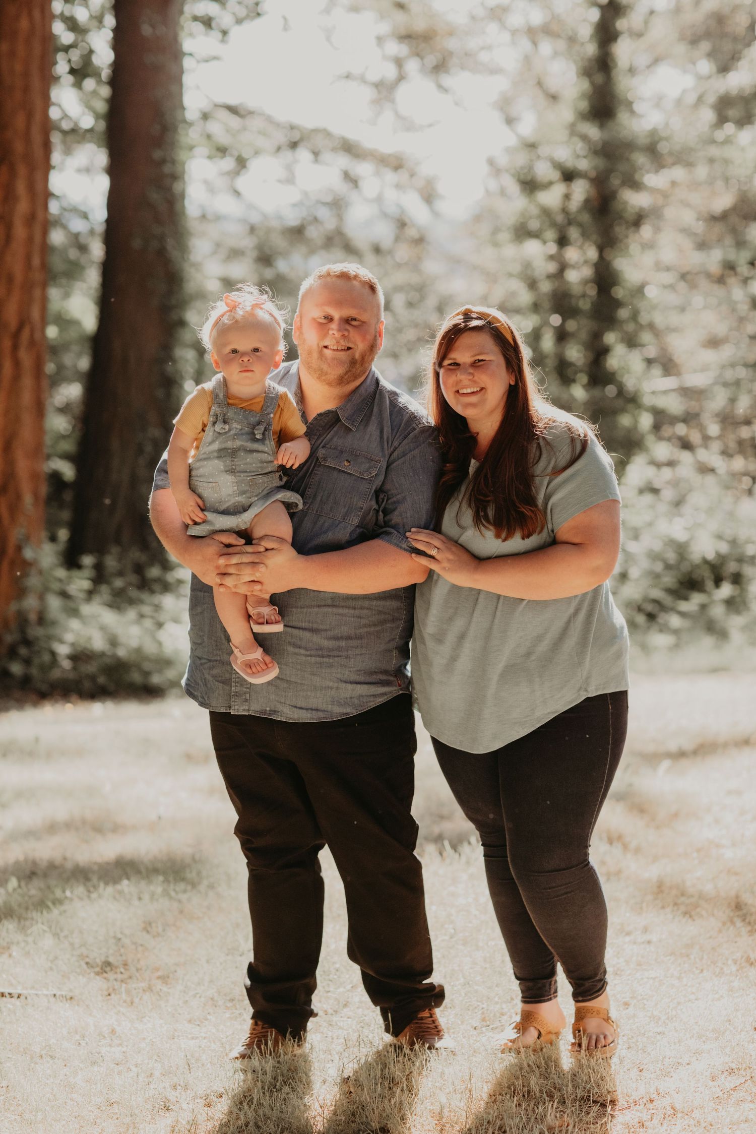 A family poses together on a sunlit forest path during a warm afternoon photoshoot.