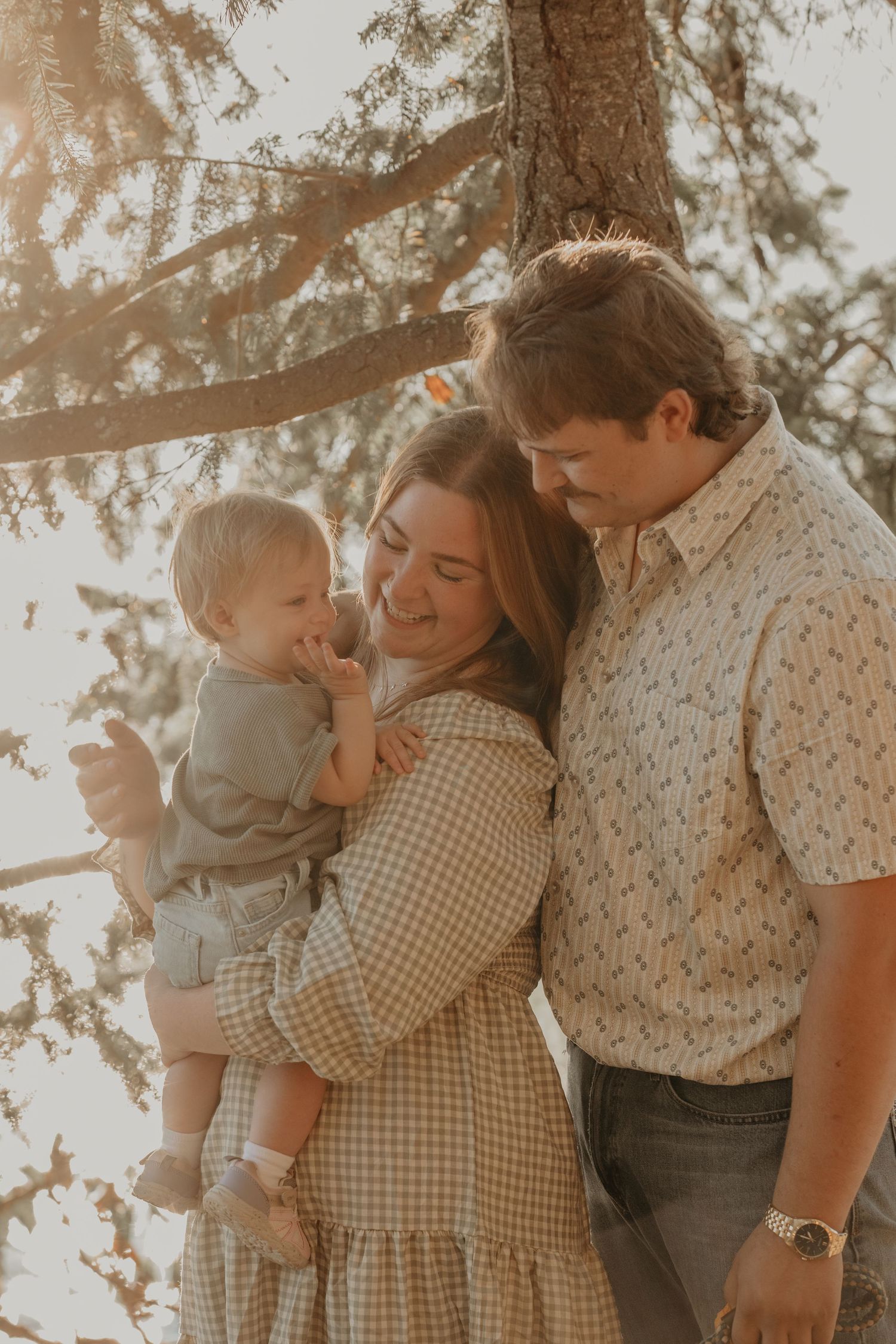 Family embraces in warm sunlight wearing vintage-style clothing during outdoor photoshoot.