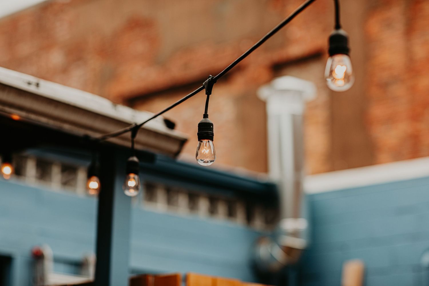 String lights hang between blue walls against a rustic brick background at dusk.
