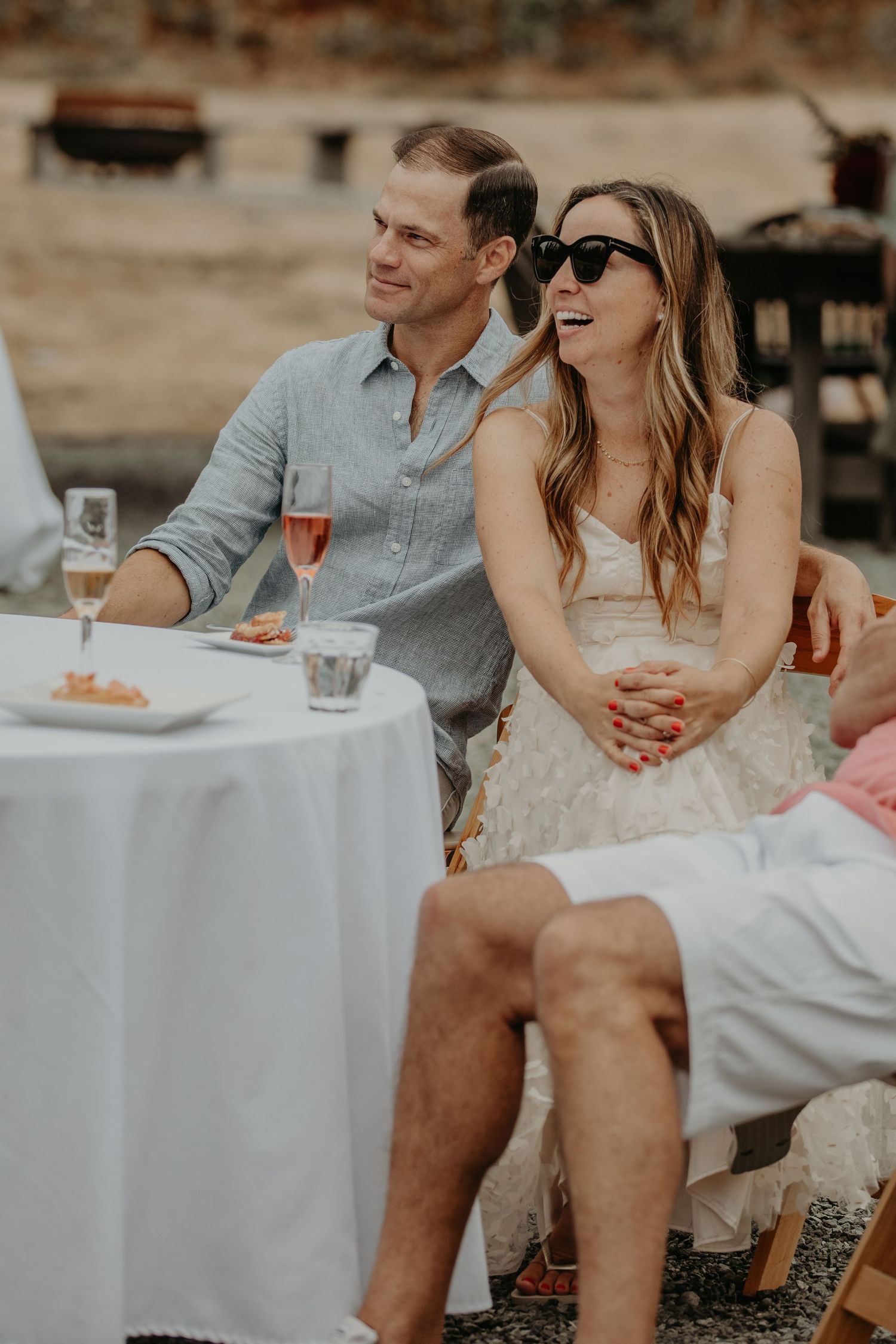 A couple enjoys an outdoor dining experience at a table with wine glasses and white tablecloth in warm evening light.