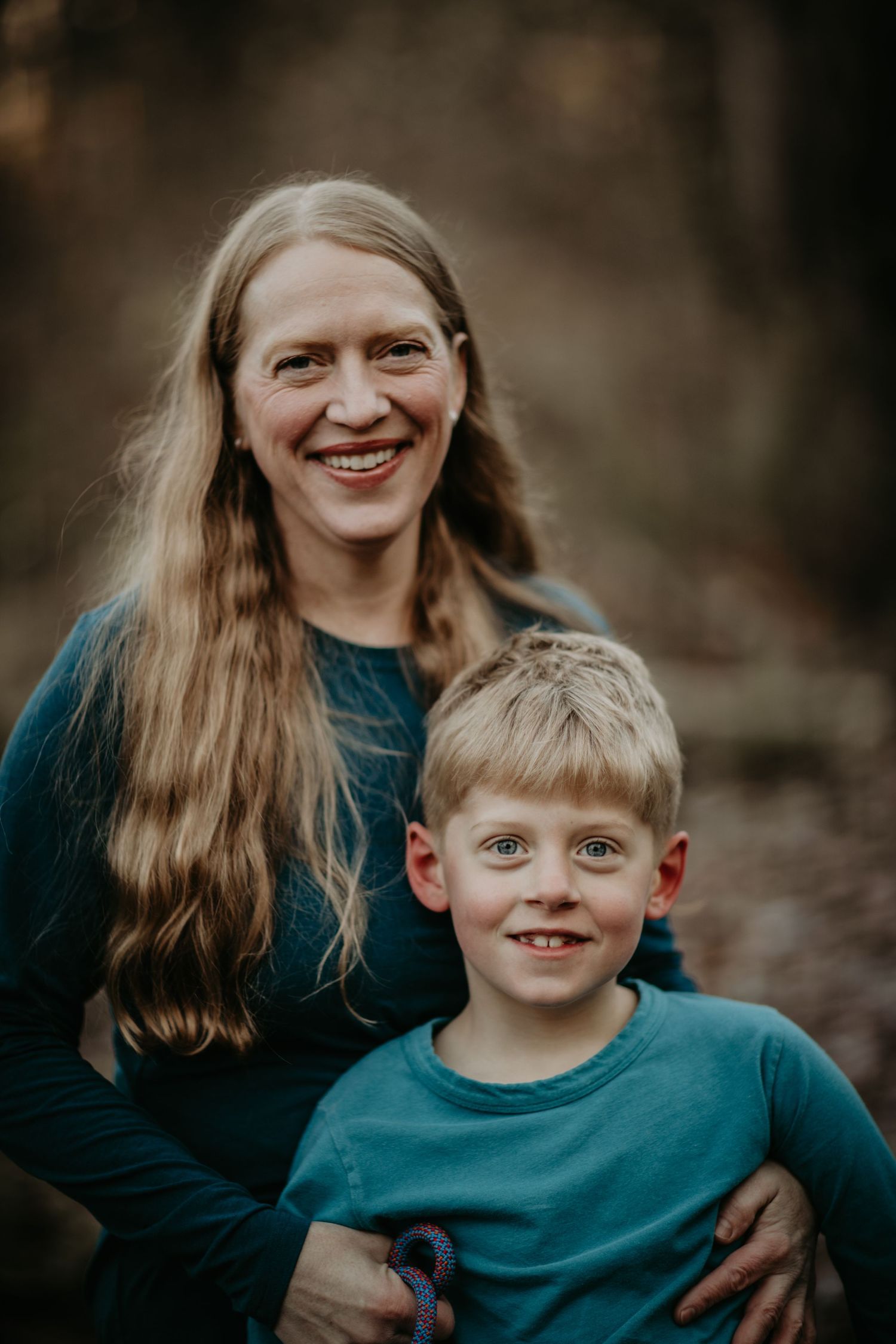 A candid portrait shows a parent and child wearing matching teal sweaters and smiling warmly outdoors.
