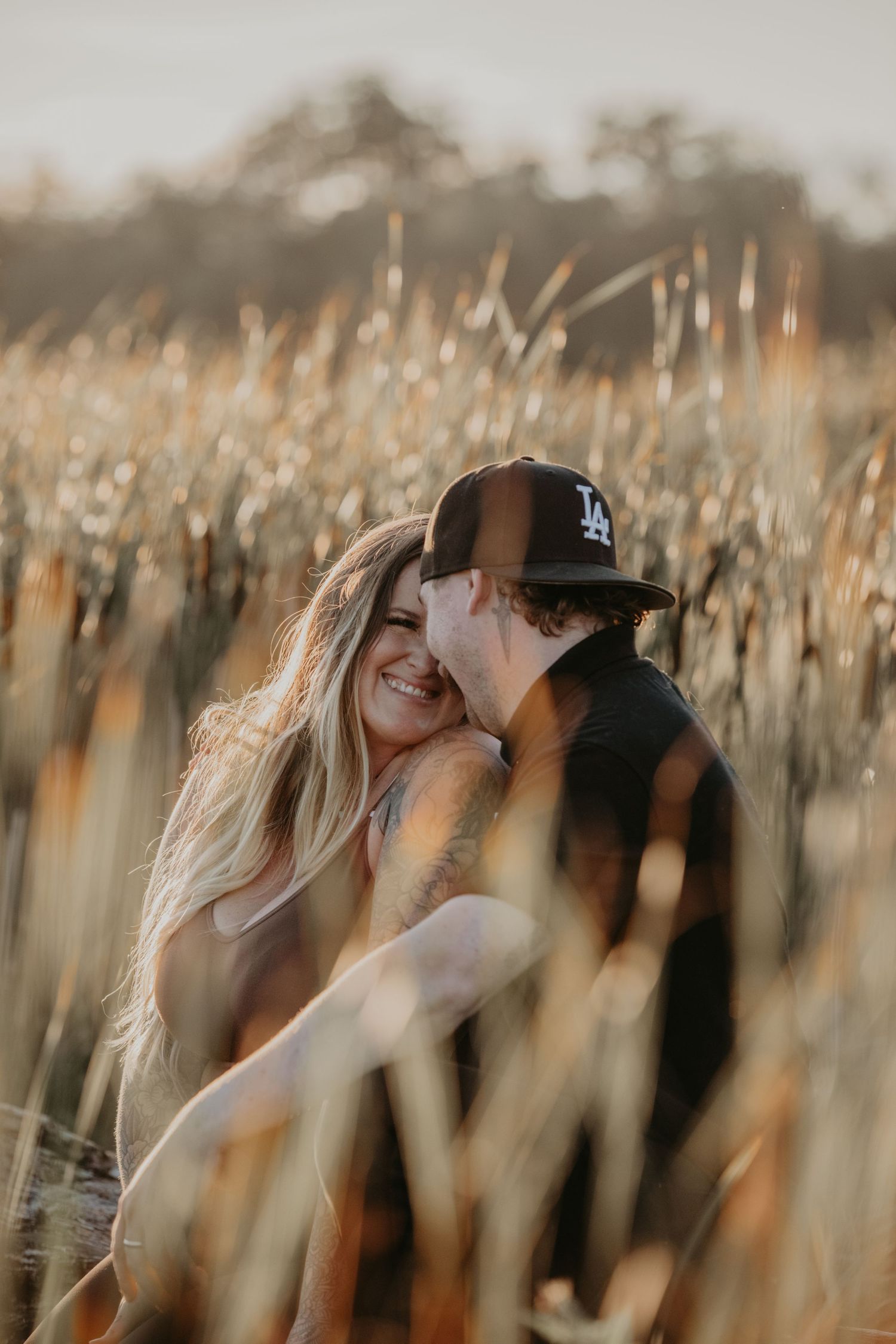 Intimate couple sharing tender moment in tall wheat field at golden hour with sunlight streaming through grass.
