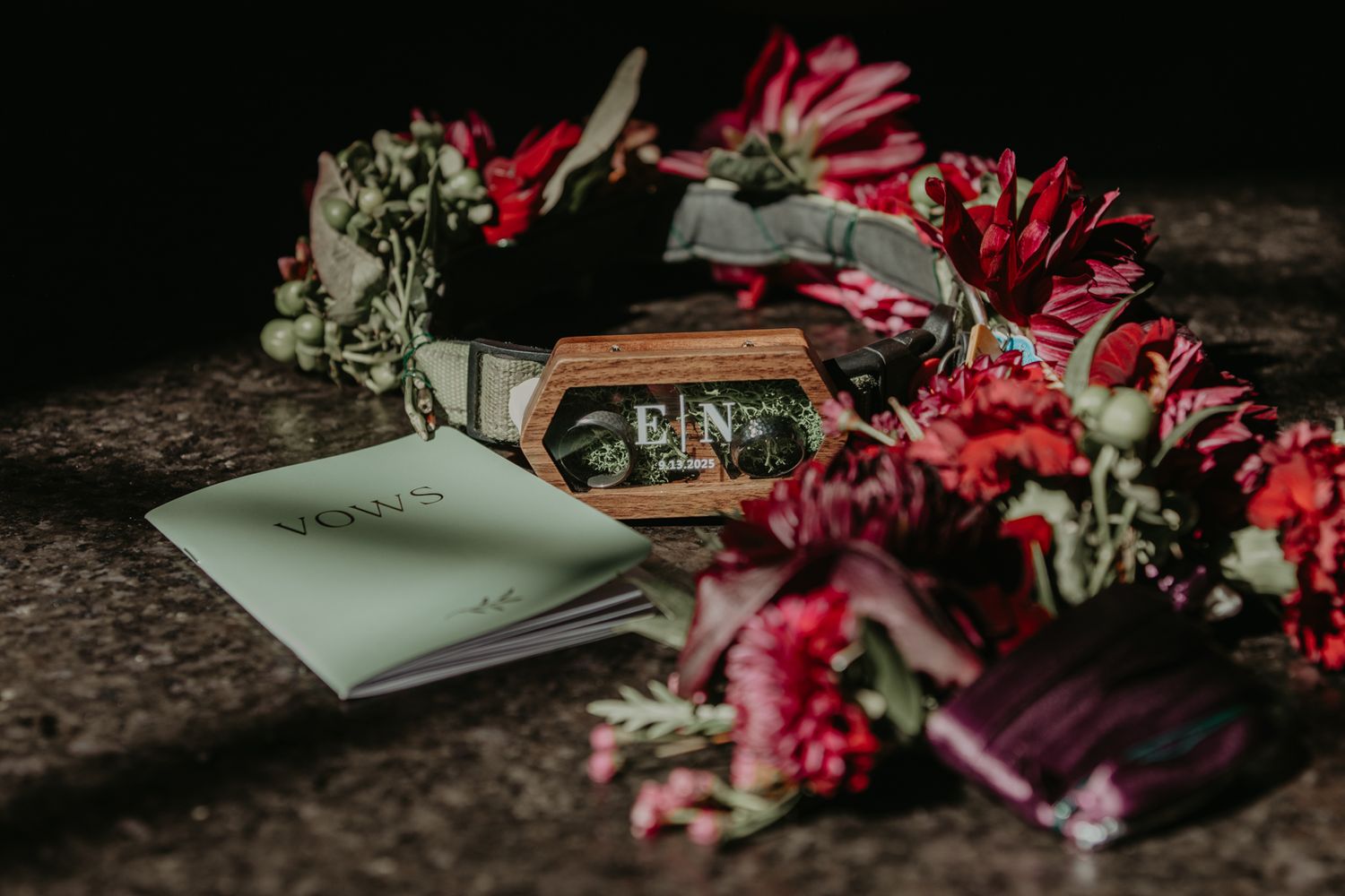 A handwritten note lies beside a circle of vibrant red gerbera daisies and baby's breath flowers on a dark surface.