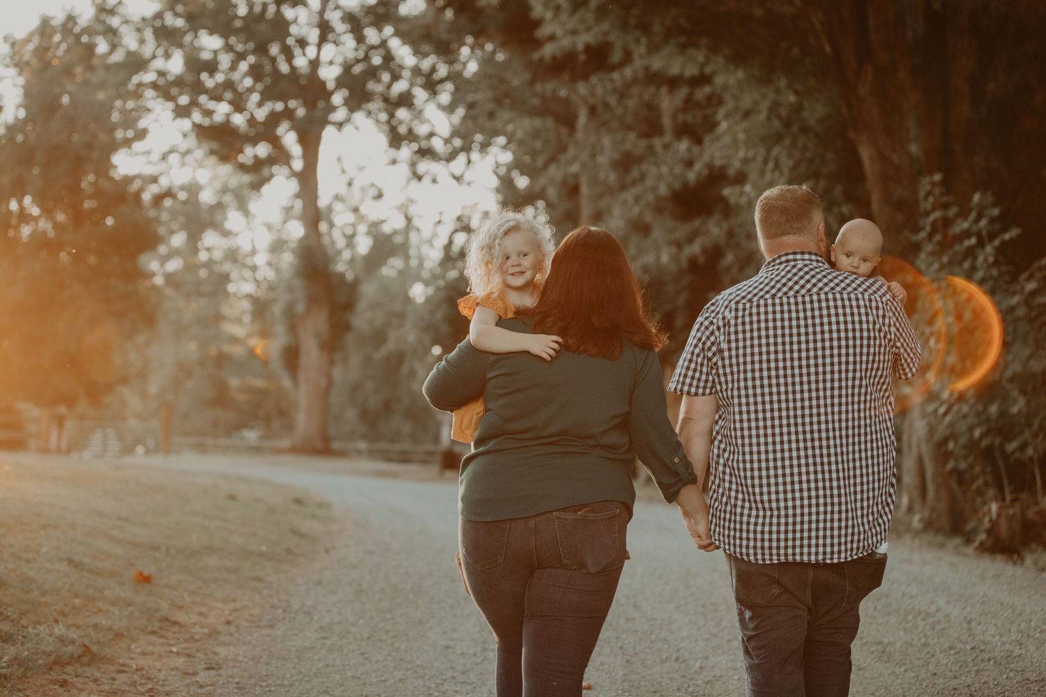 A couple walks together down a sunlit path during golden hour as they hold hands and enjoy the outdoors.